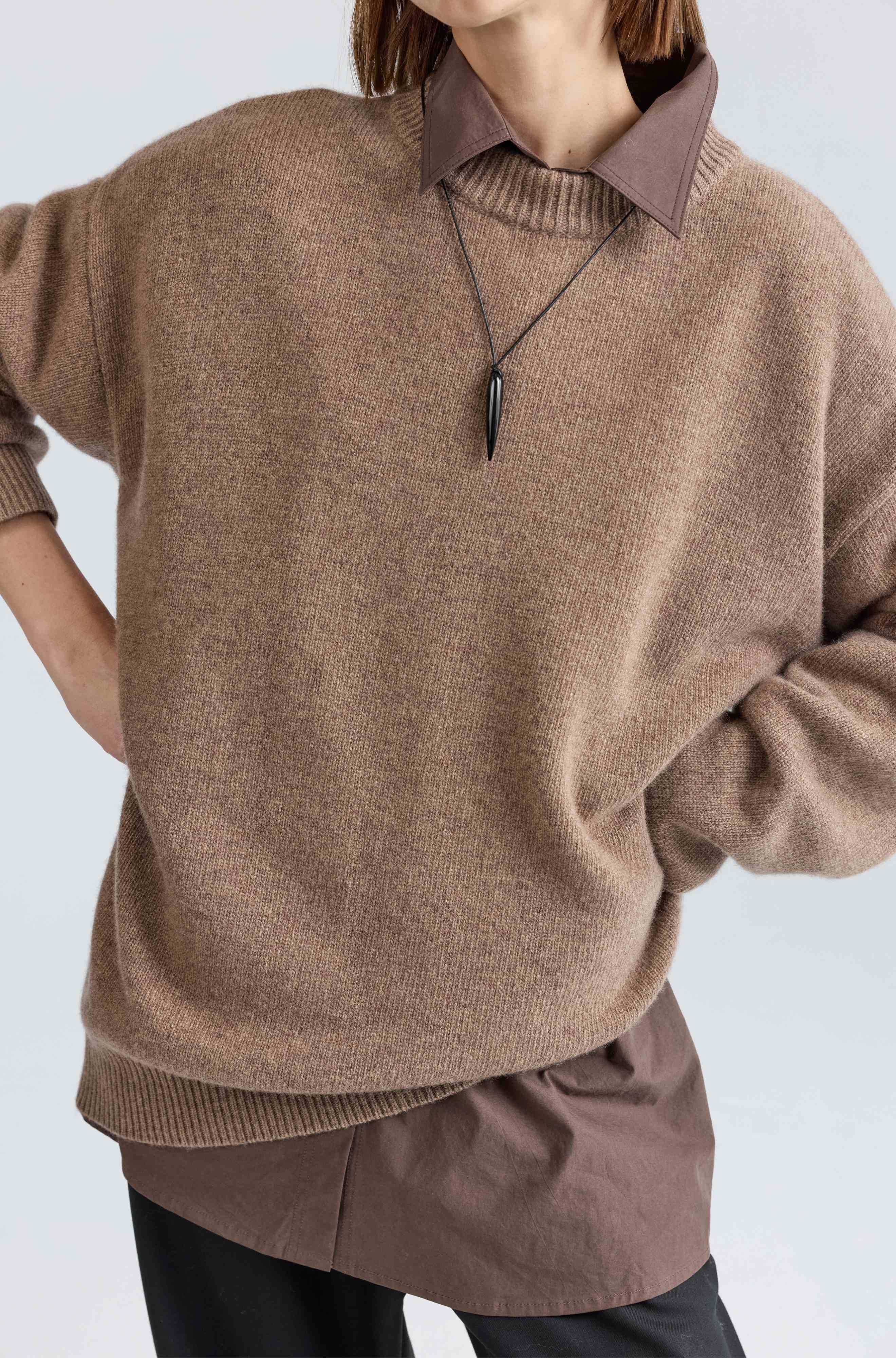 Person wearing a brown sweater and pants with a plain background