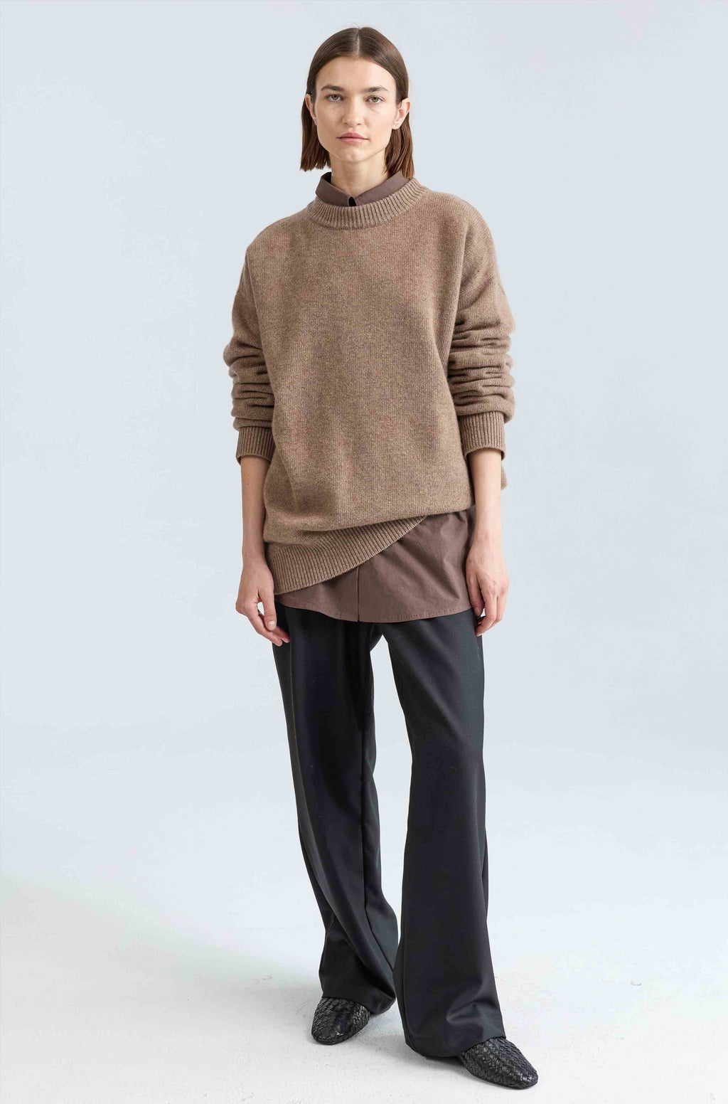 Person wearing a brown sweater and black pants on a light gray background