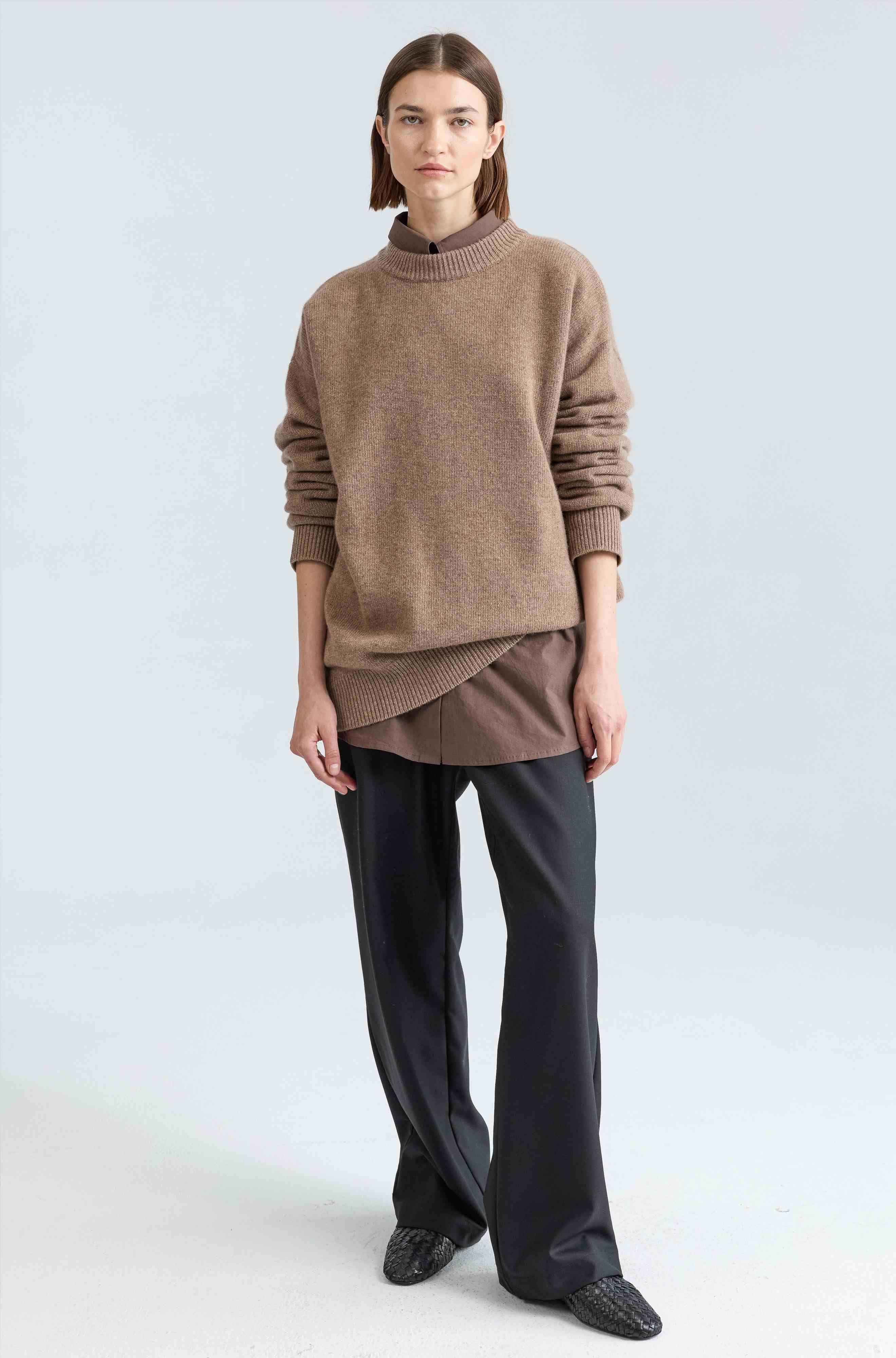 Person wearing a brown sweater and black pants on a light gray background