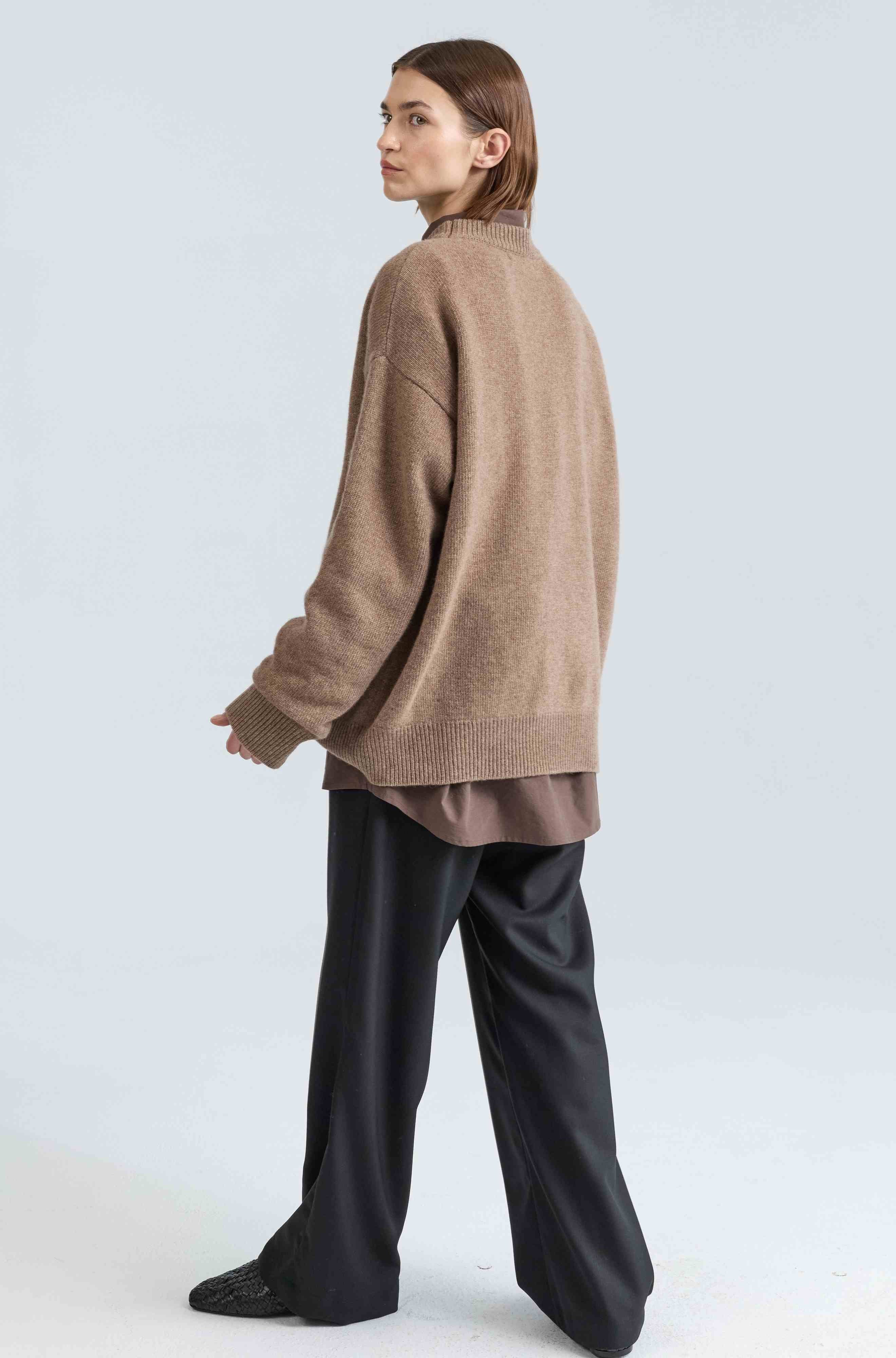 Person wearing a brown sweater and black pants on a white background