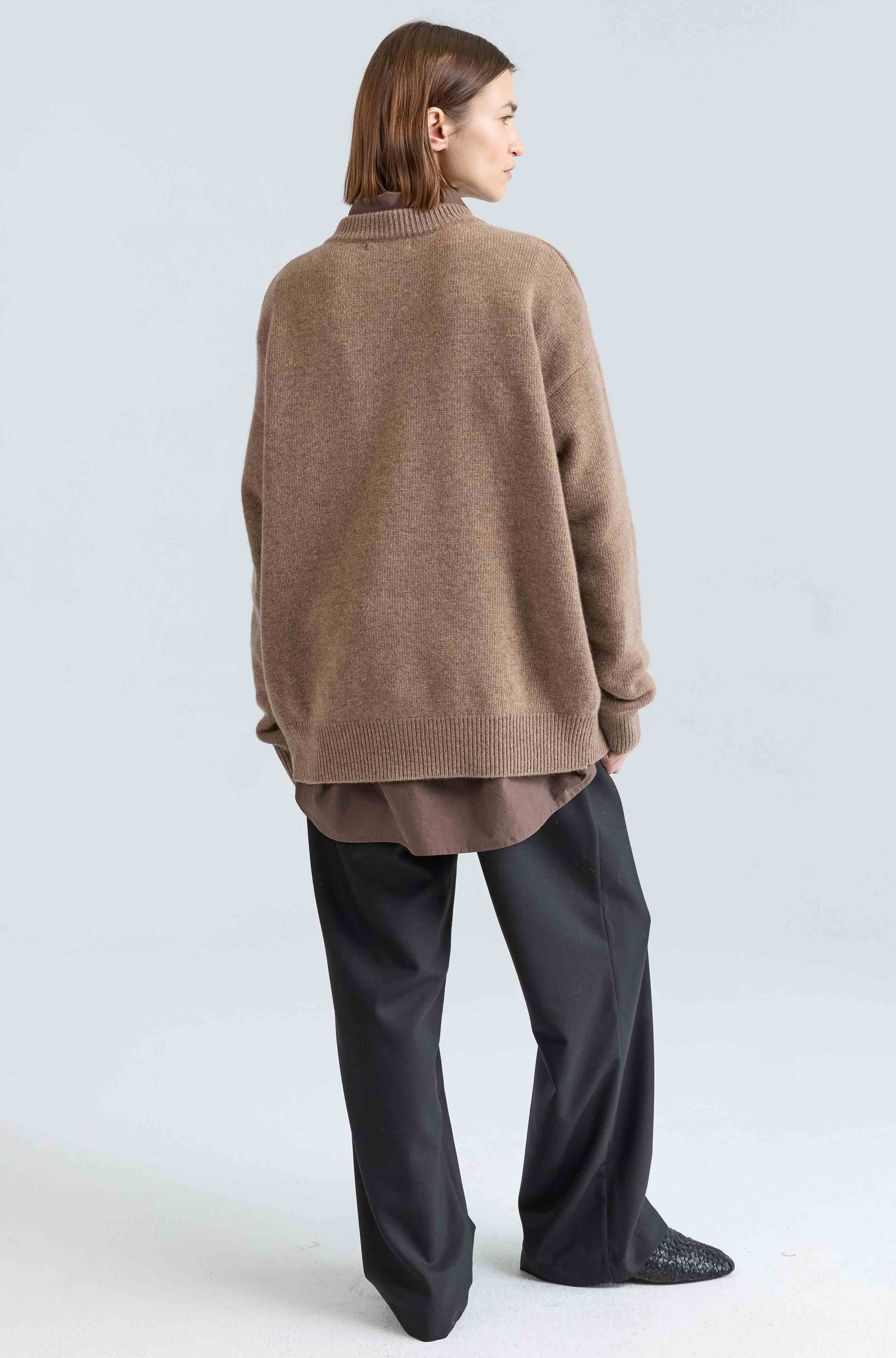 Person wearing a brown sweater and black pants on a white background