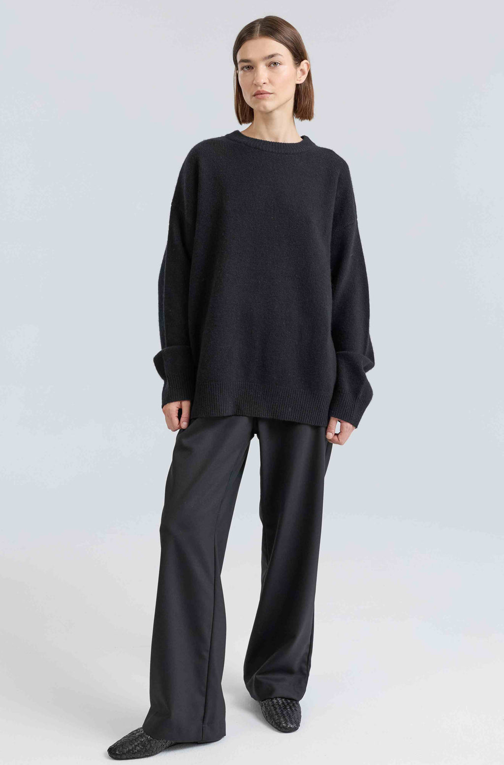 Person wearing a black sweater and pants on a light gray background