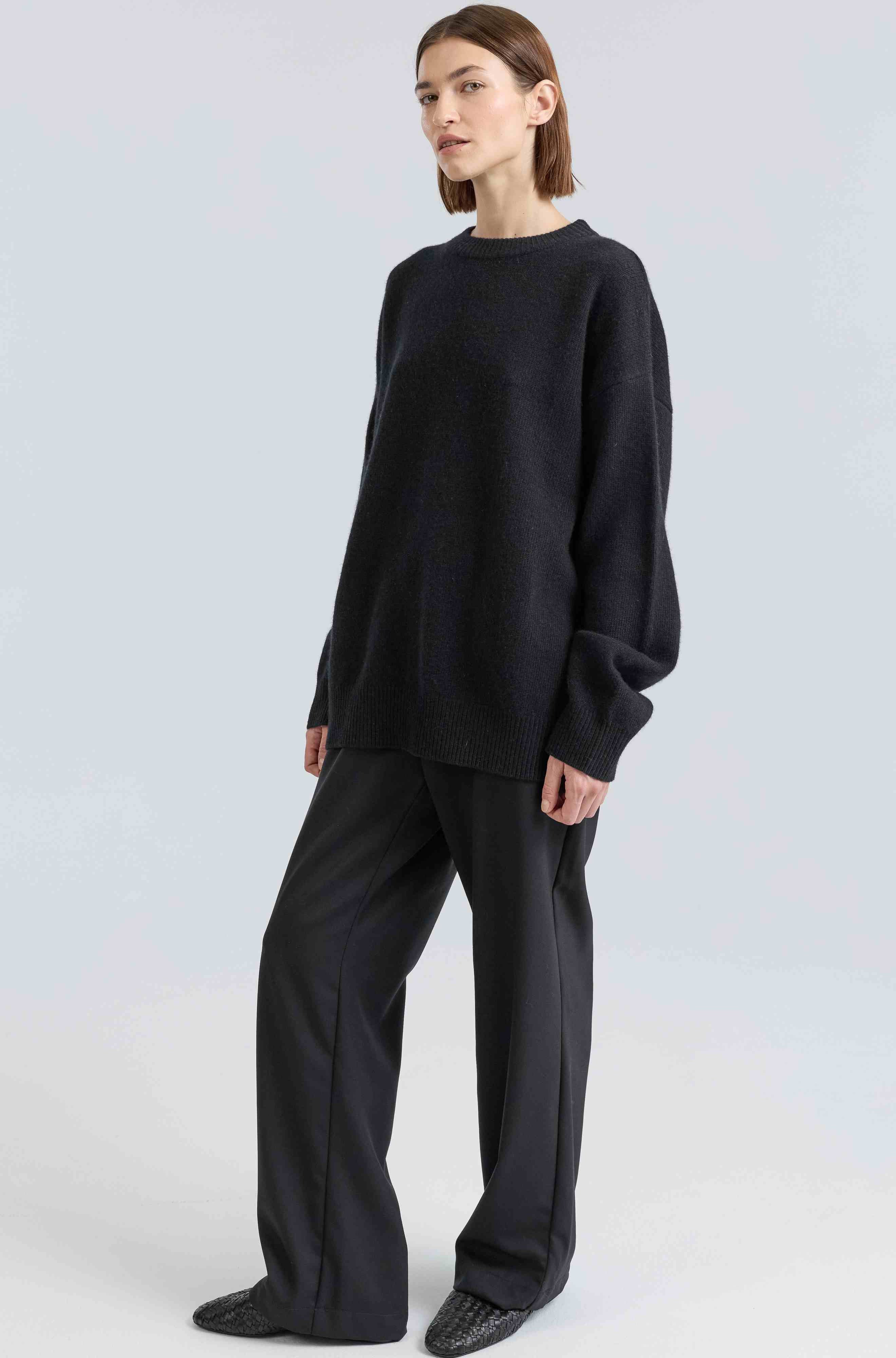Person wearing a black sweater and pants on a white background