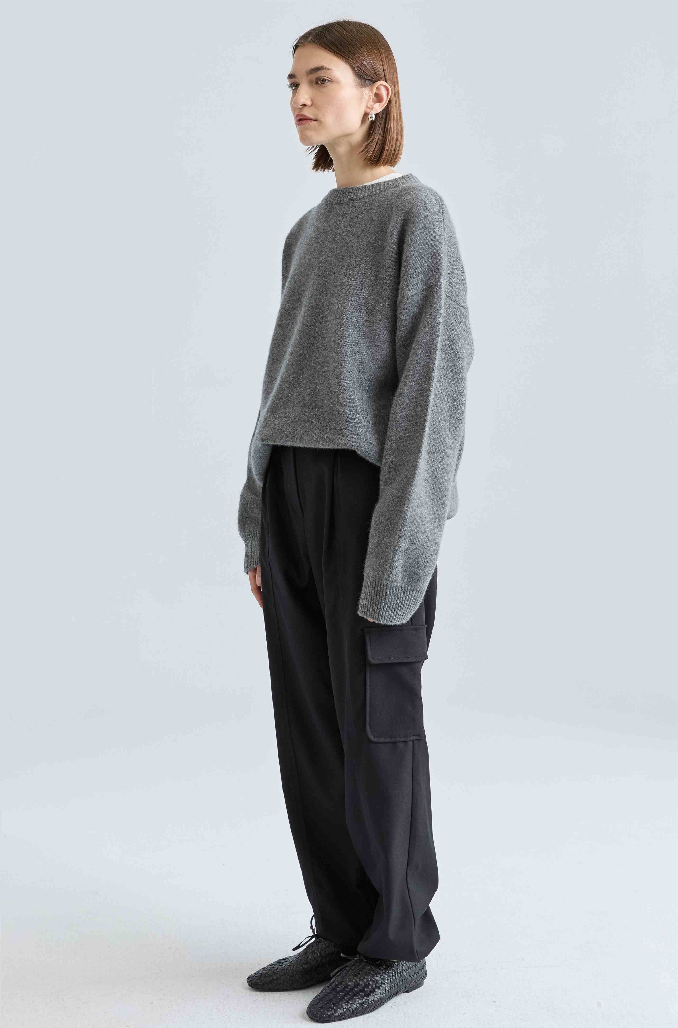 Person wearing a gray sweater and black pants on a white background