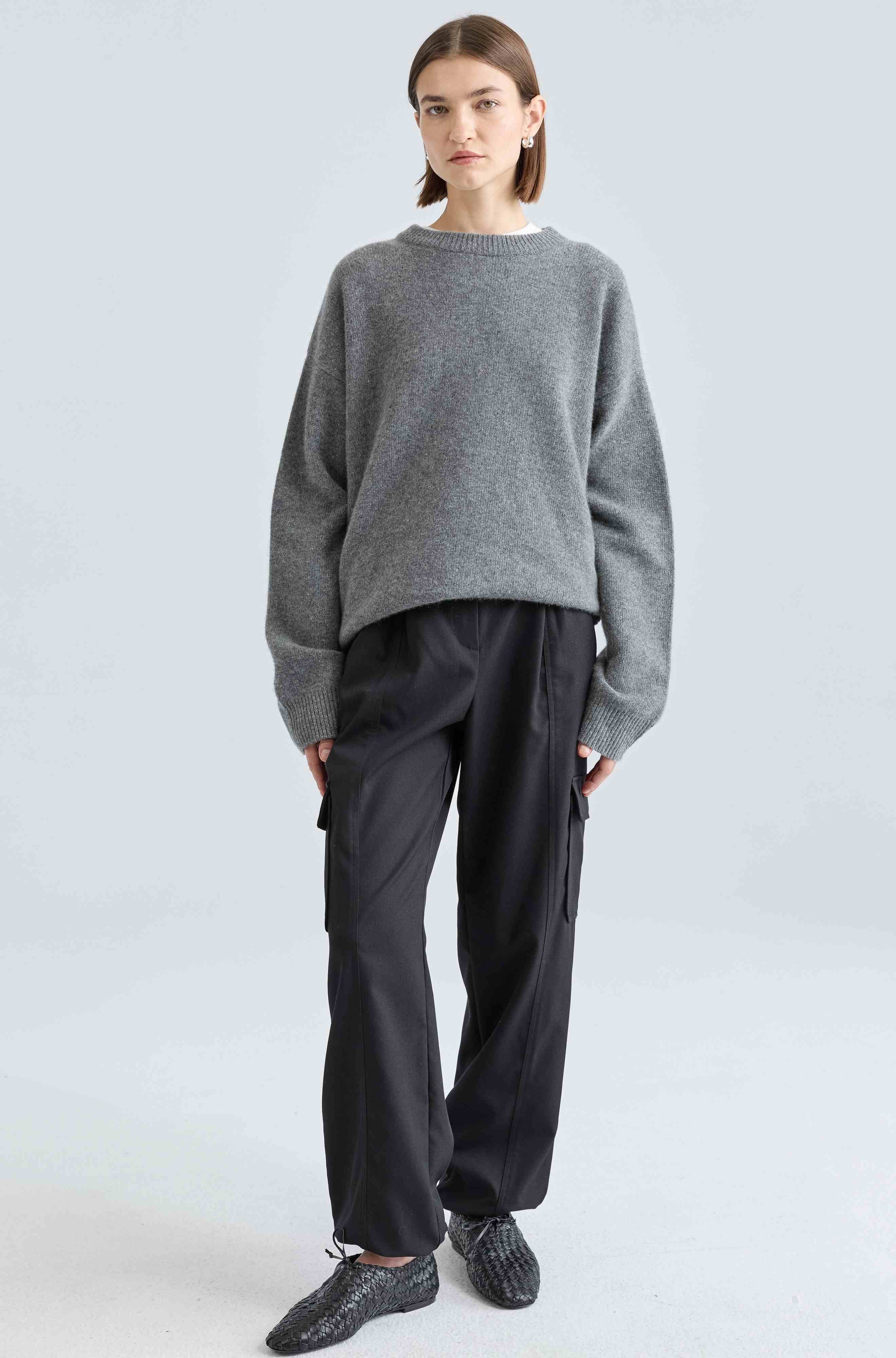 Person wearing a gray sweater and black pants on a light gray background