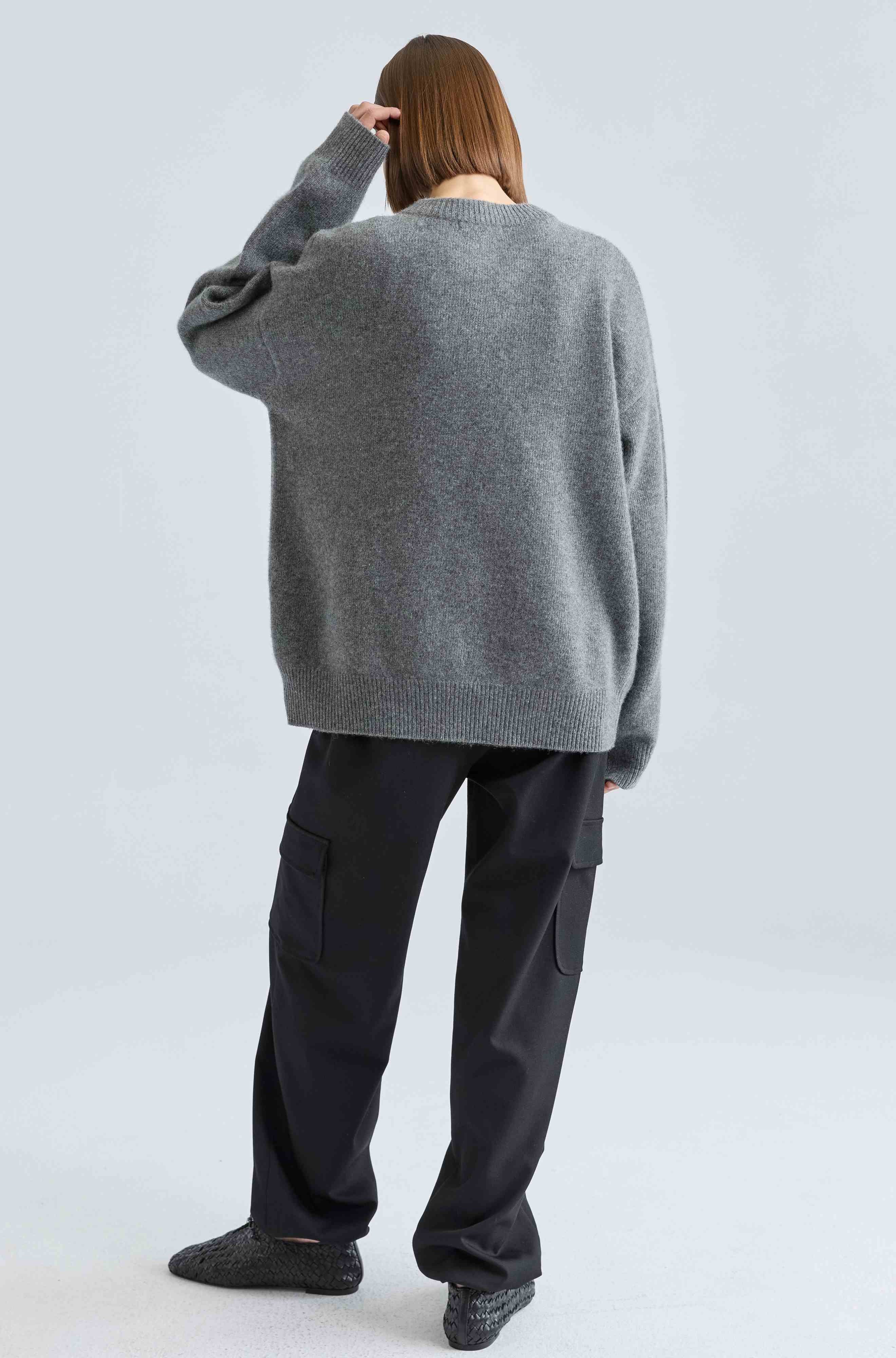 Person wearing a gray sweater and black pants on a light gray background