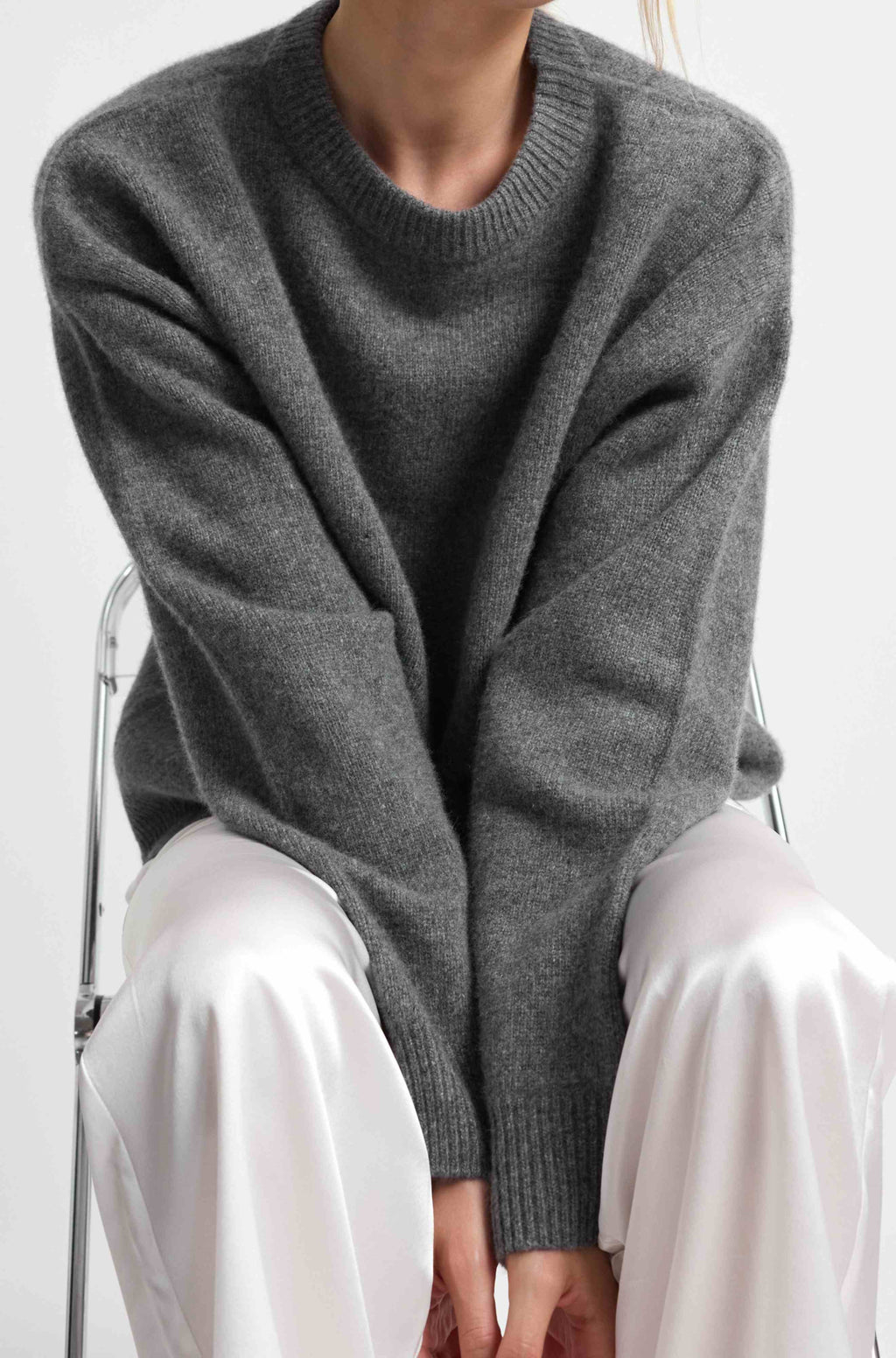 Person wearing a gray sweater and white pants on a white background