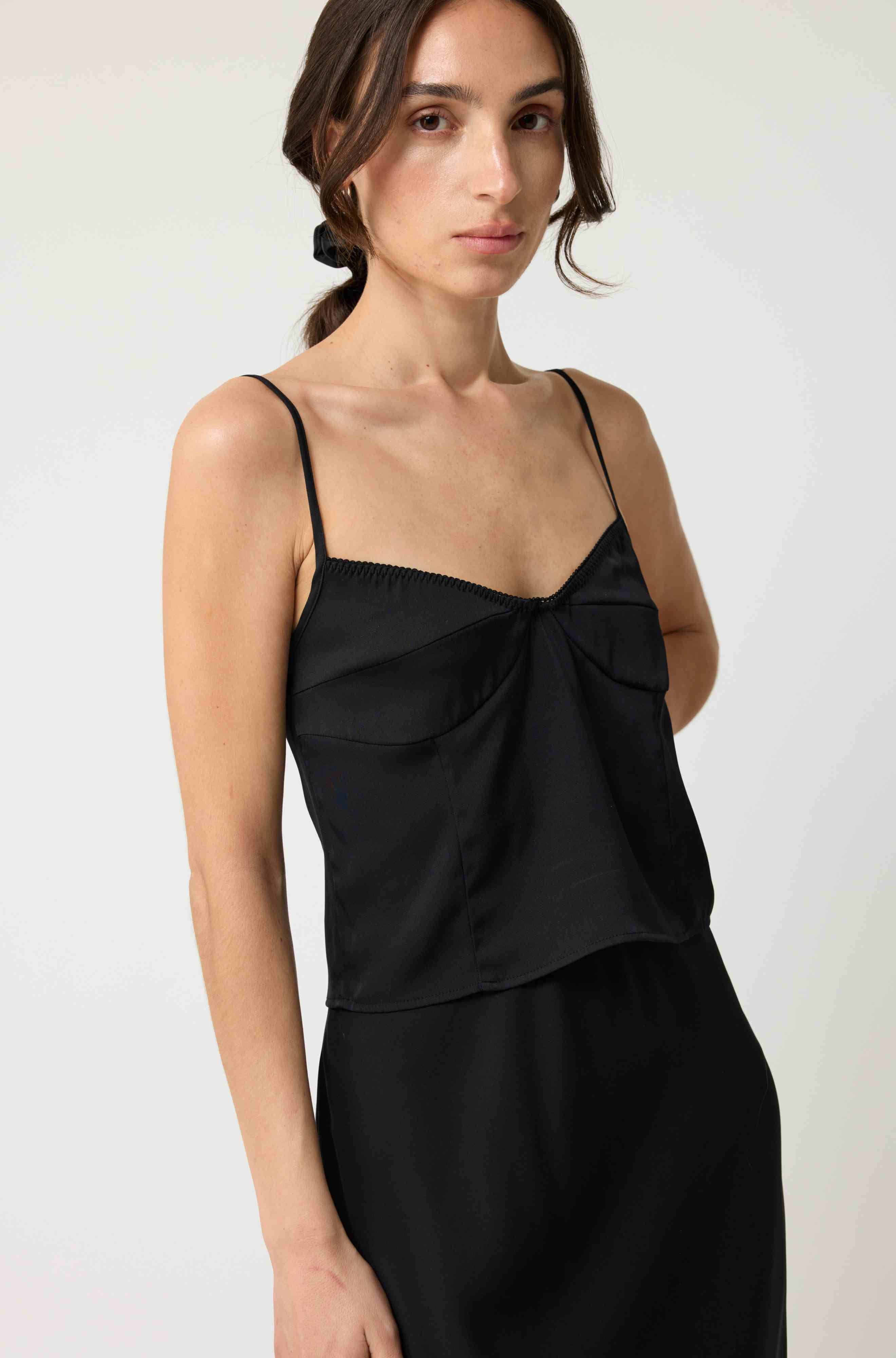 Woman wearing a black silk top and skirt set against a white background