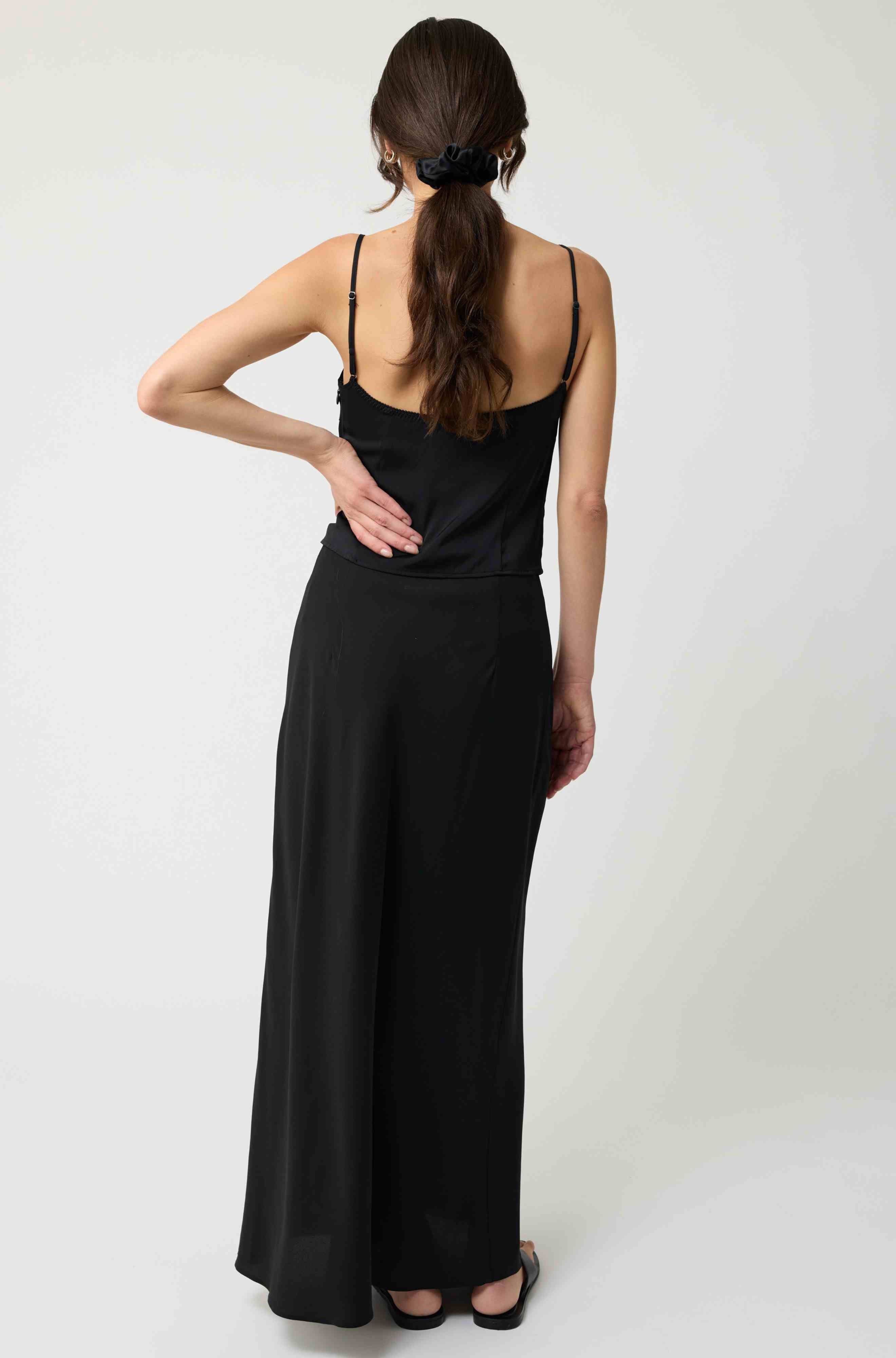 Woman wearing a black silk top and skirt set standing against a white background