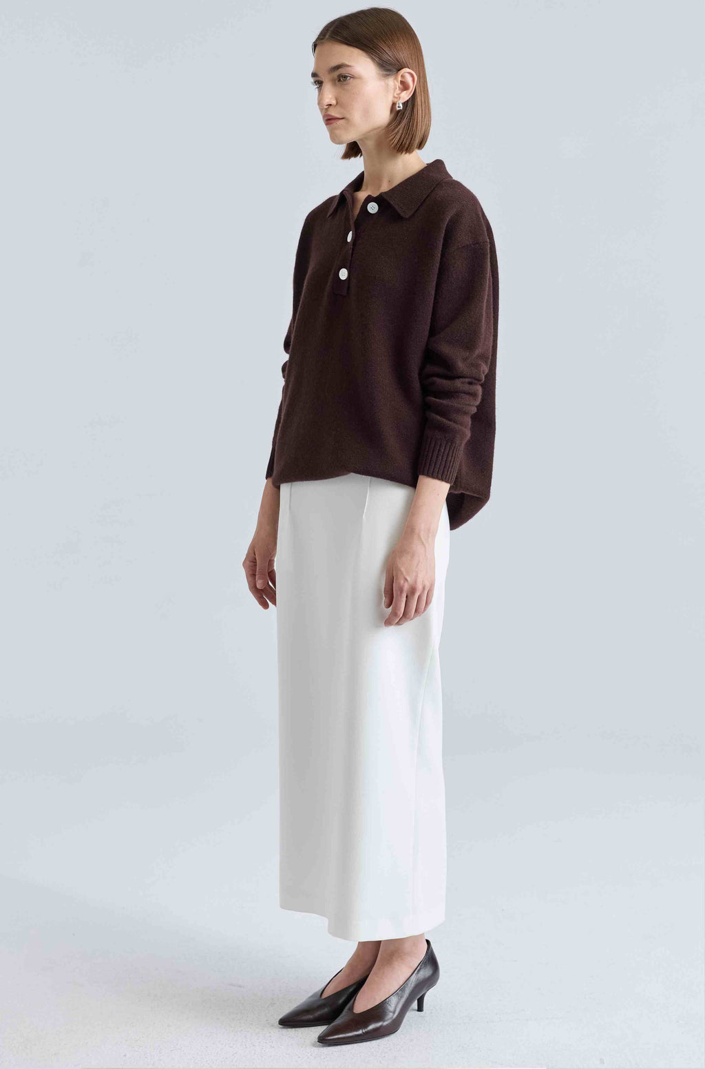 Woman wearing a brown shirt and white skirt on a light gray background