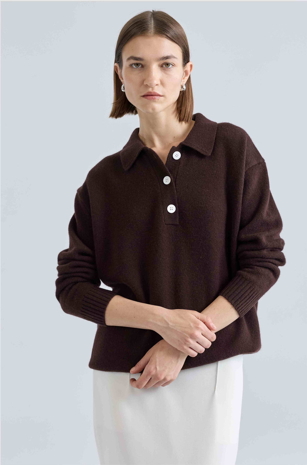 Woman wearing a brown sweater with white buttons on a light gray background
