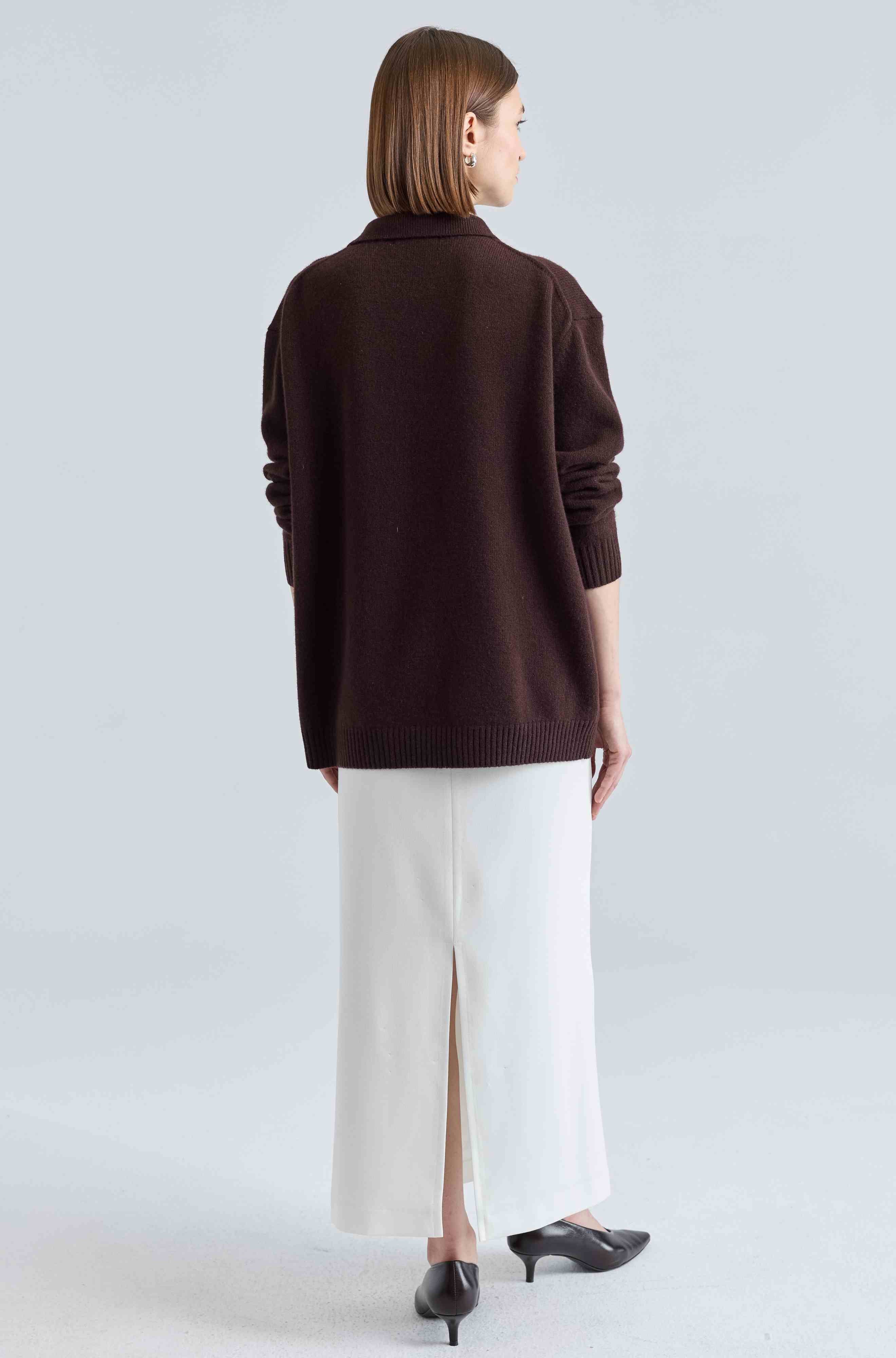 Woman wearing a brown sweater and white skirt on a light gray background