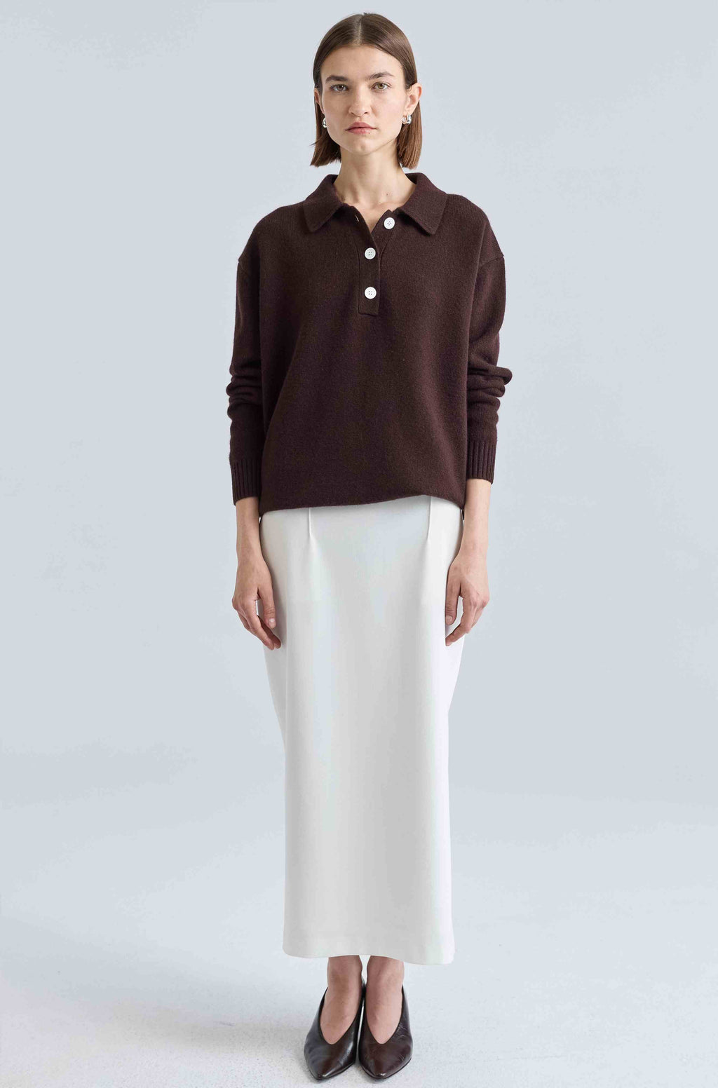 Woman wearing a brown sweater and white skirt on a light gray background