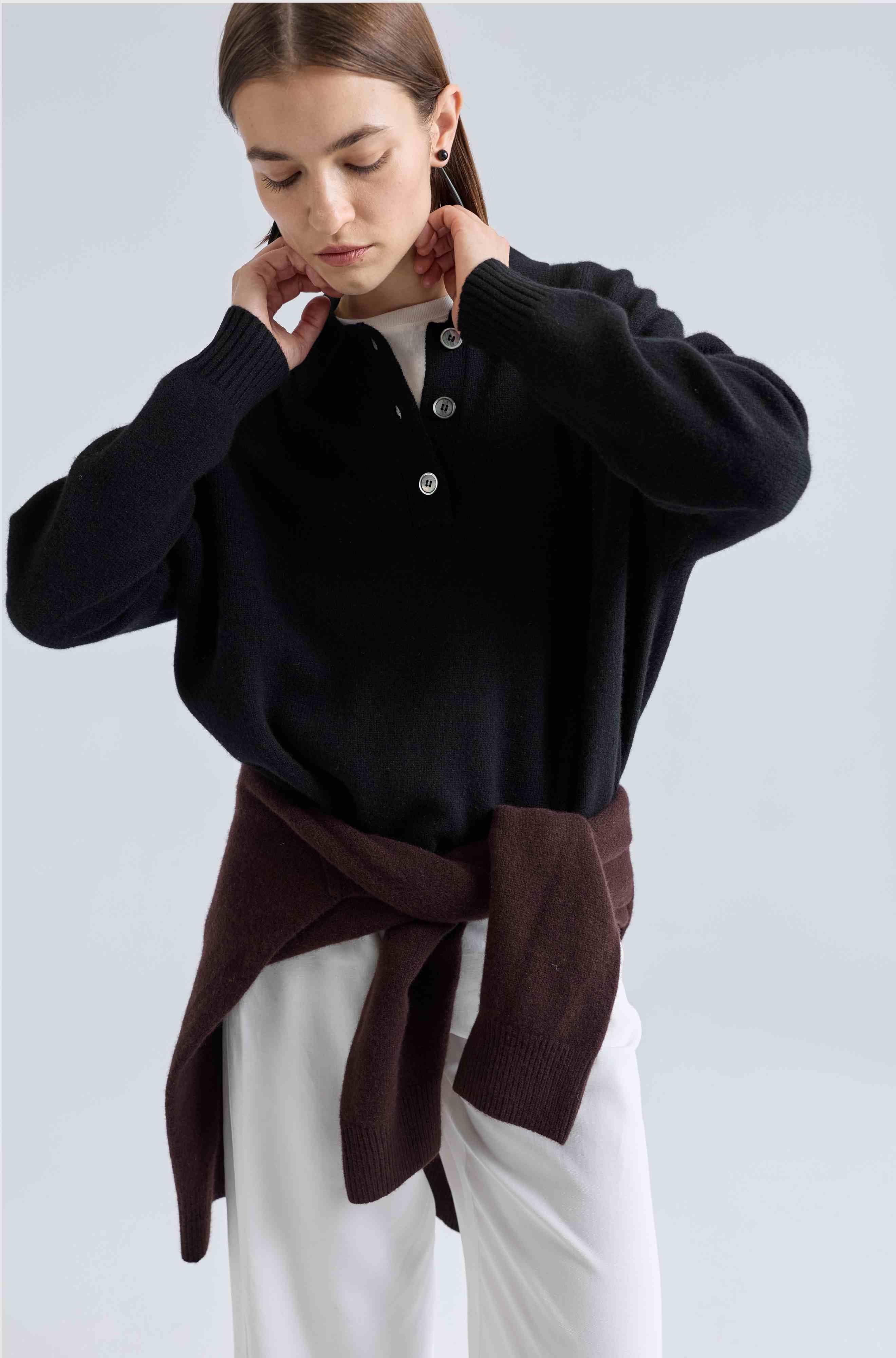 Woman wearing a black sweater with a brown scarf against a light gray background