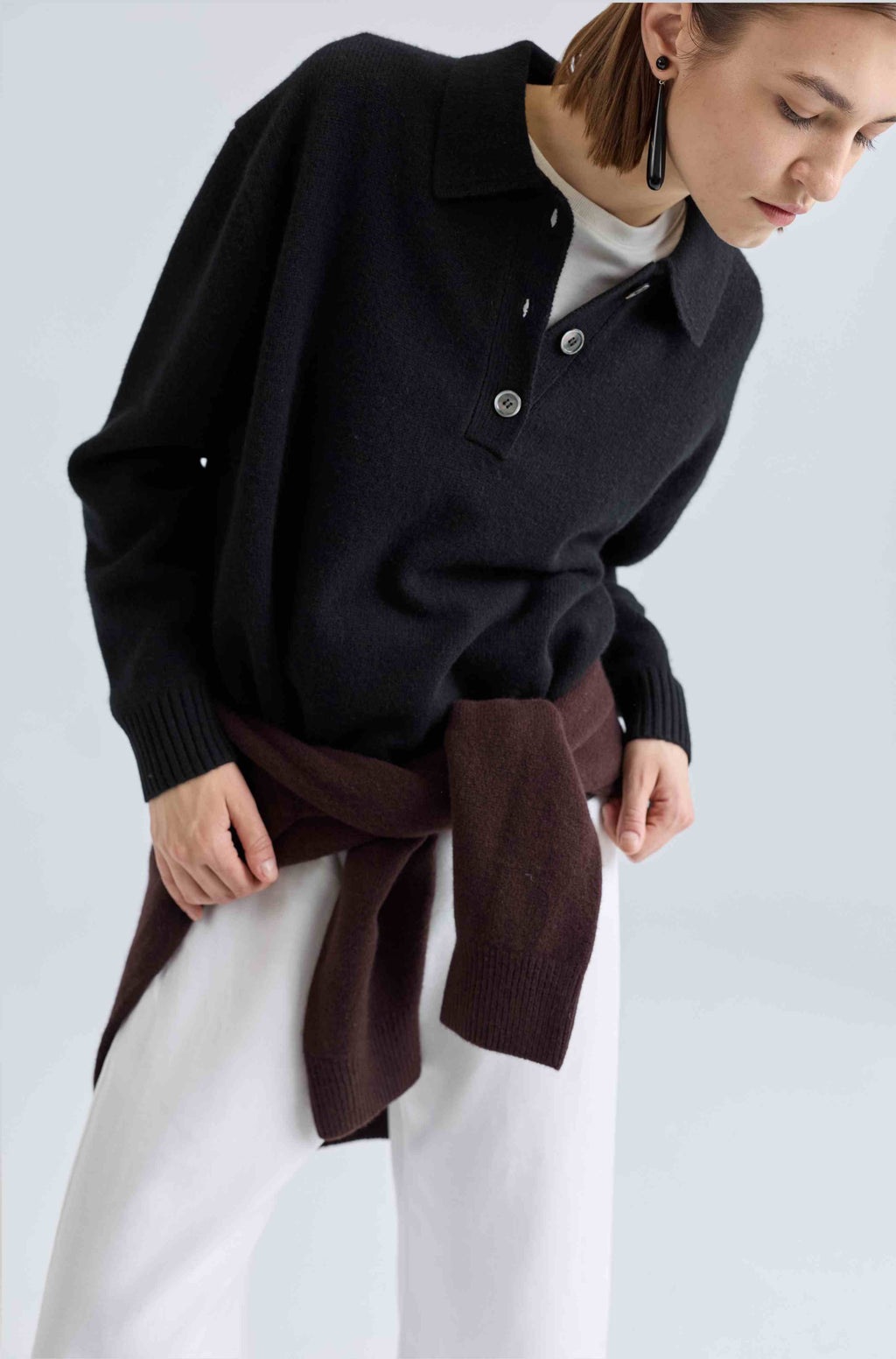 Person wearing a black sweater with a brown sweater tied around her waist over a white shirt on a light gray background