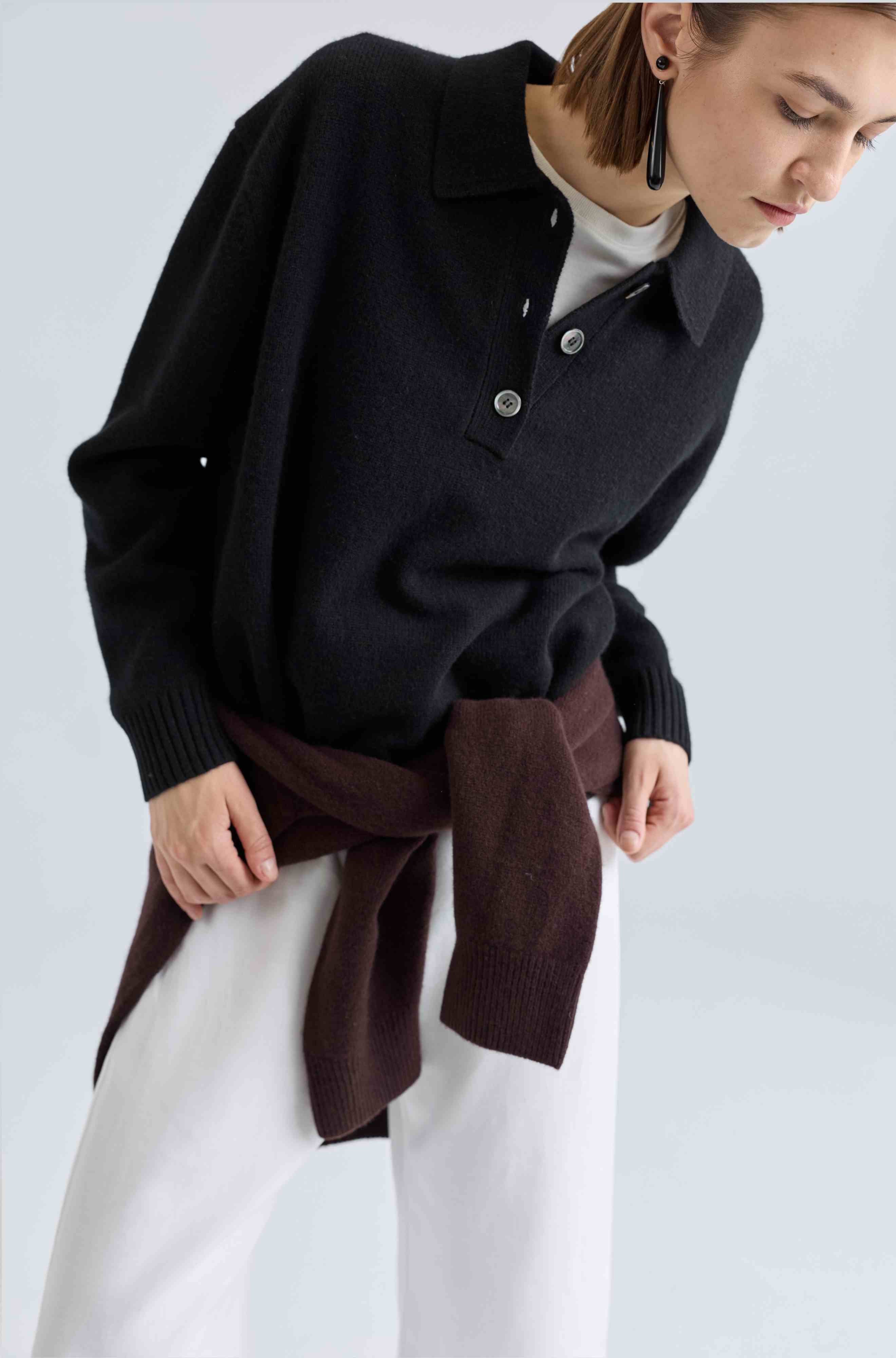 Person wearing a black sweater with a brown sweater tied around her waist over a white shirt on a light gray background