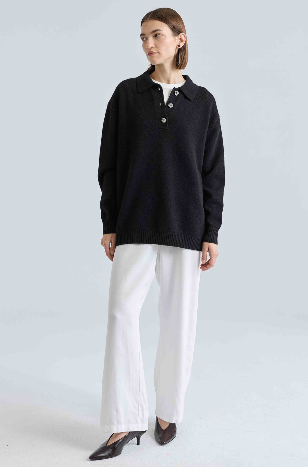 Woman wearing a black sweater and white pants on a light gray background