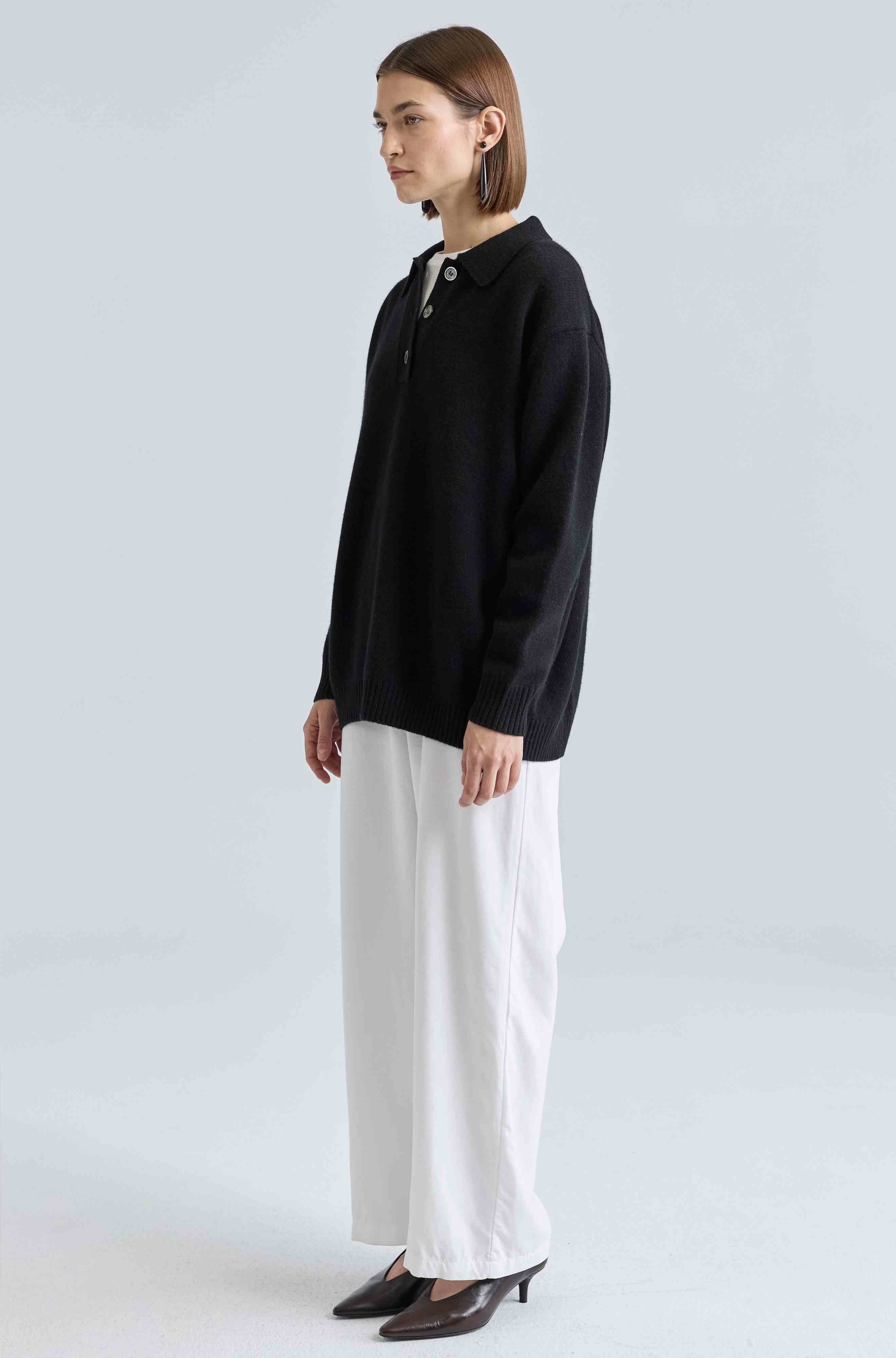 Person wearing a black sweater and white pants on a light gray background