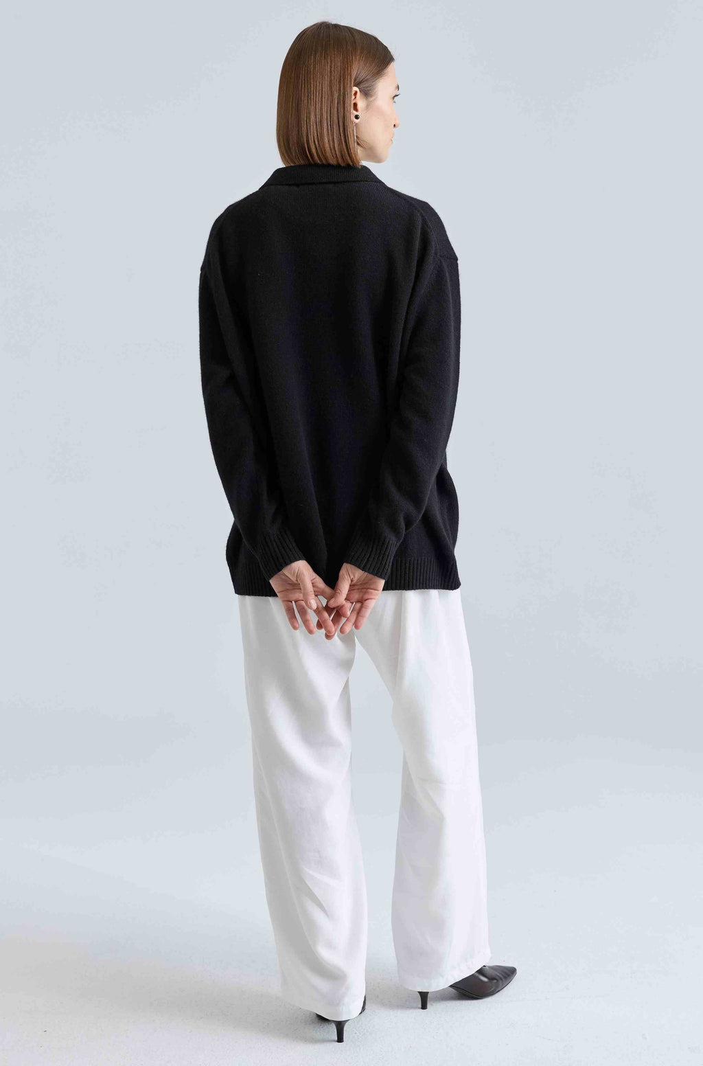 Person wearing a black sweater and white pants on a light gray background