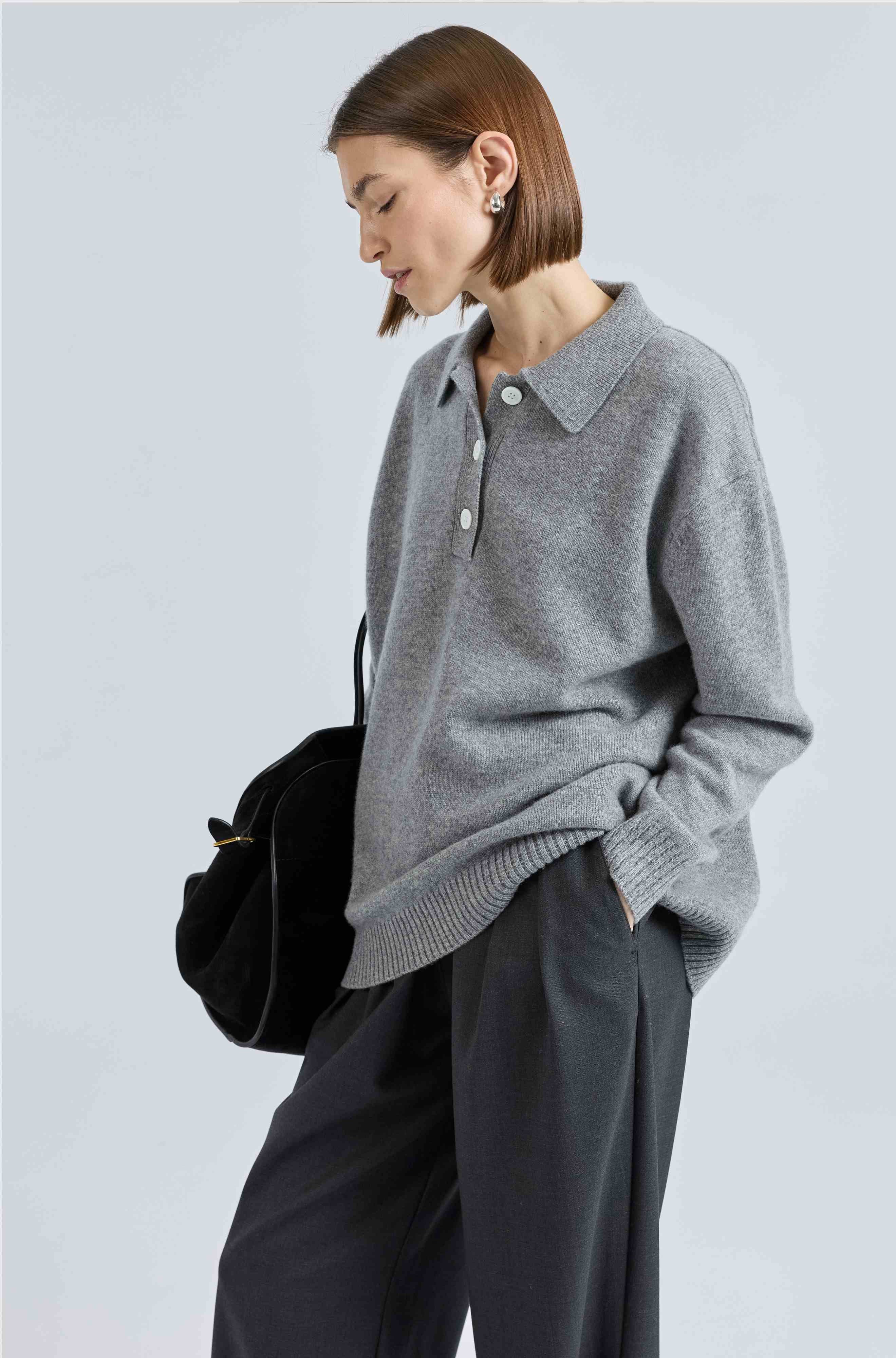 Woman wearing a gray sweater and dark pants against a light background