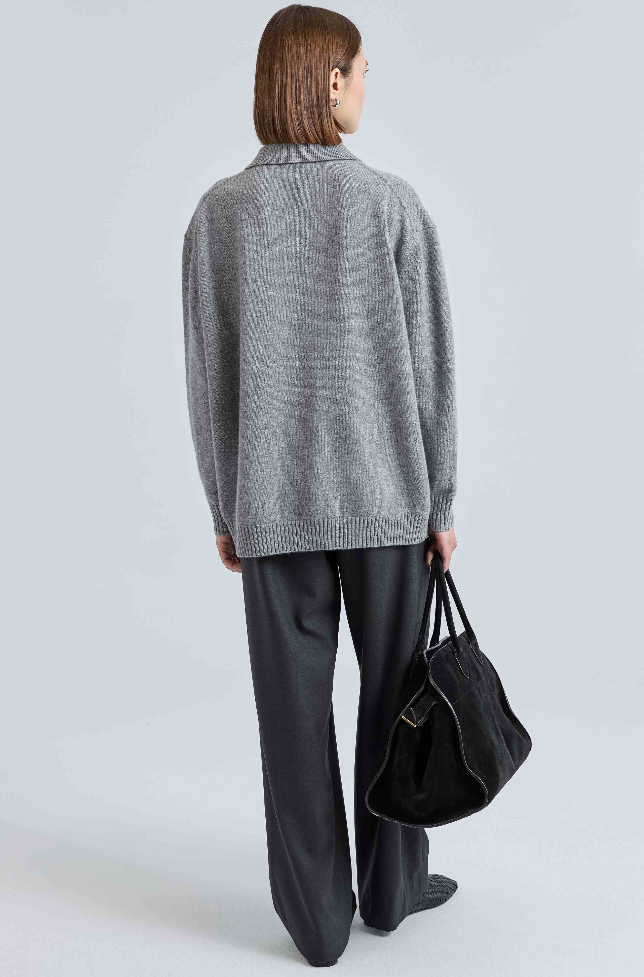 Person wearing a gray sweater and black pants holding a black bag on a light gray background