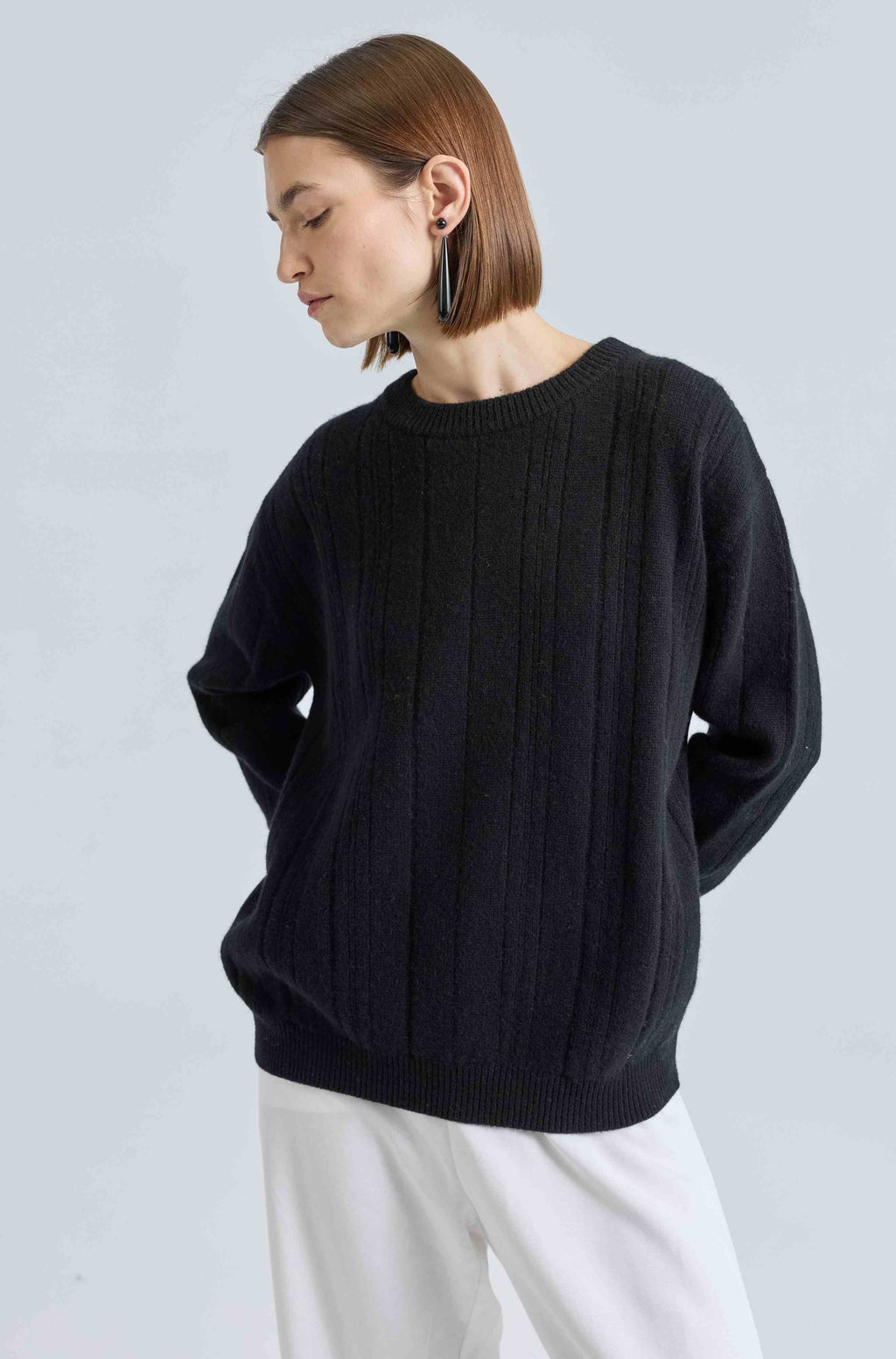 Woman wearing a black sweater and white pants against a light gray background