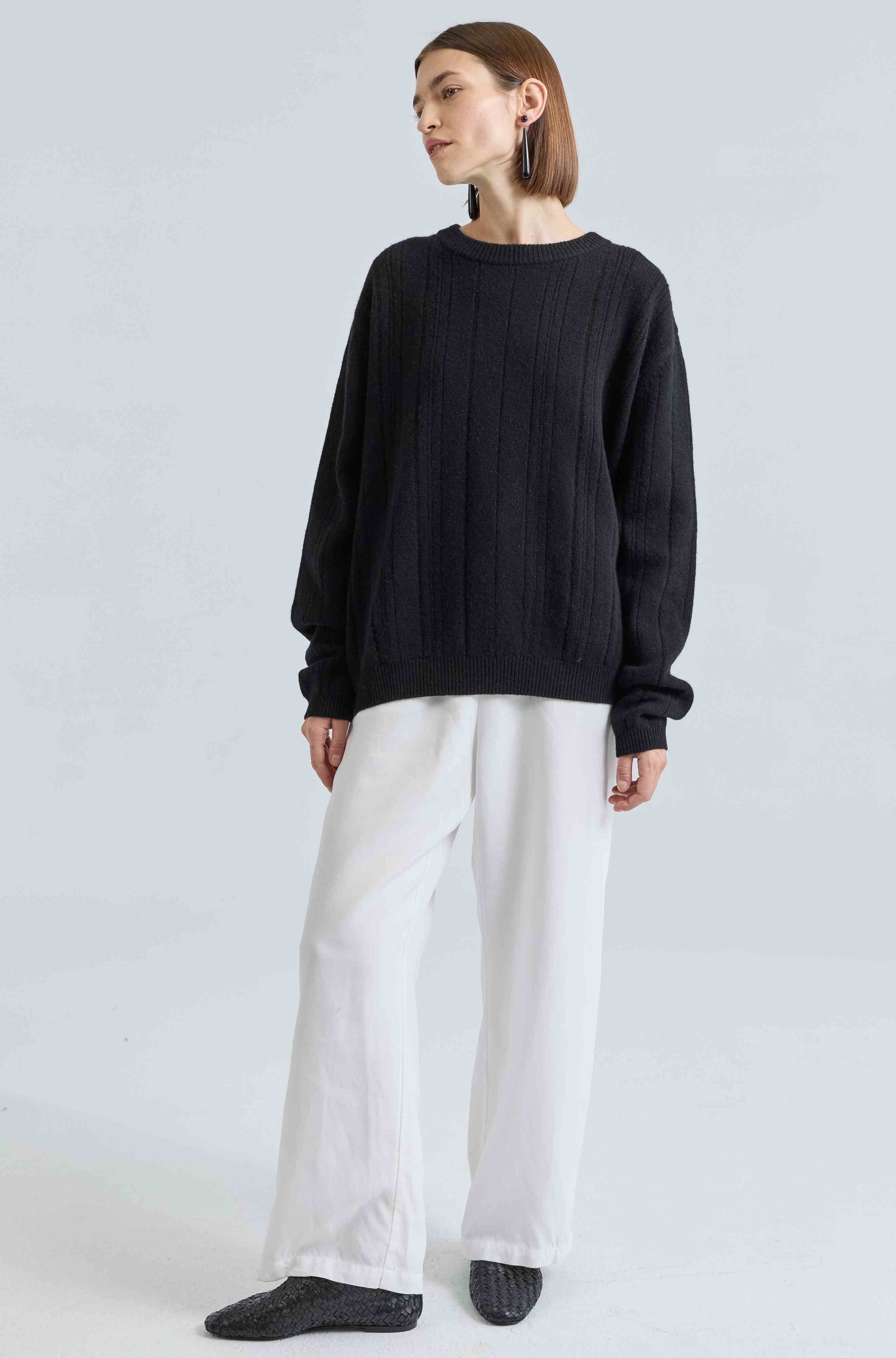 Person wearing a black sweater and white pants on a light gray background