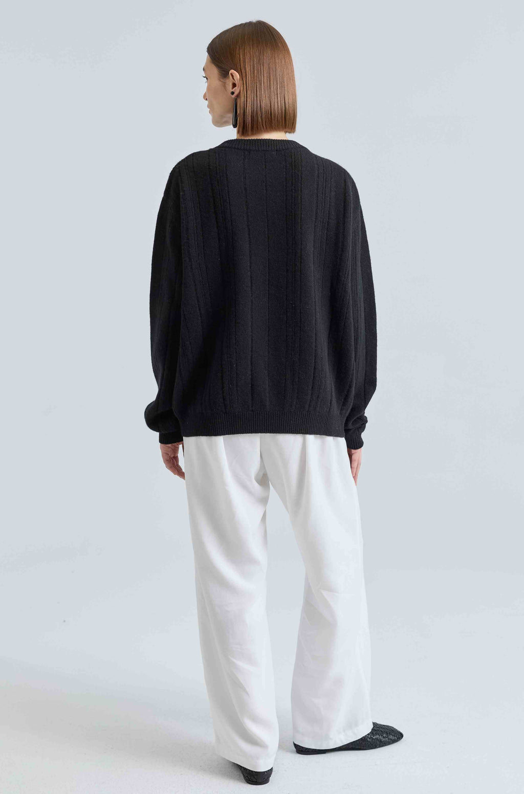 Person wearing a black sweater and white pants on a light gray background