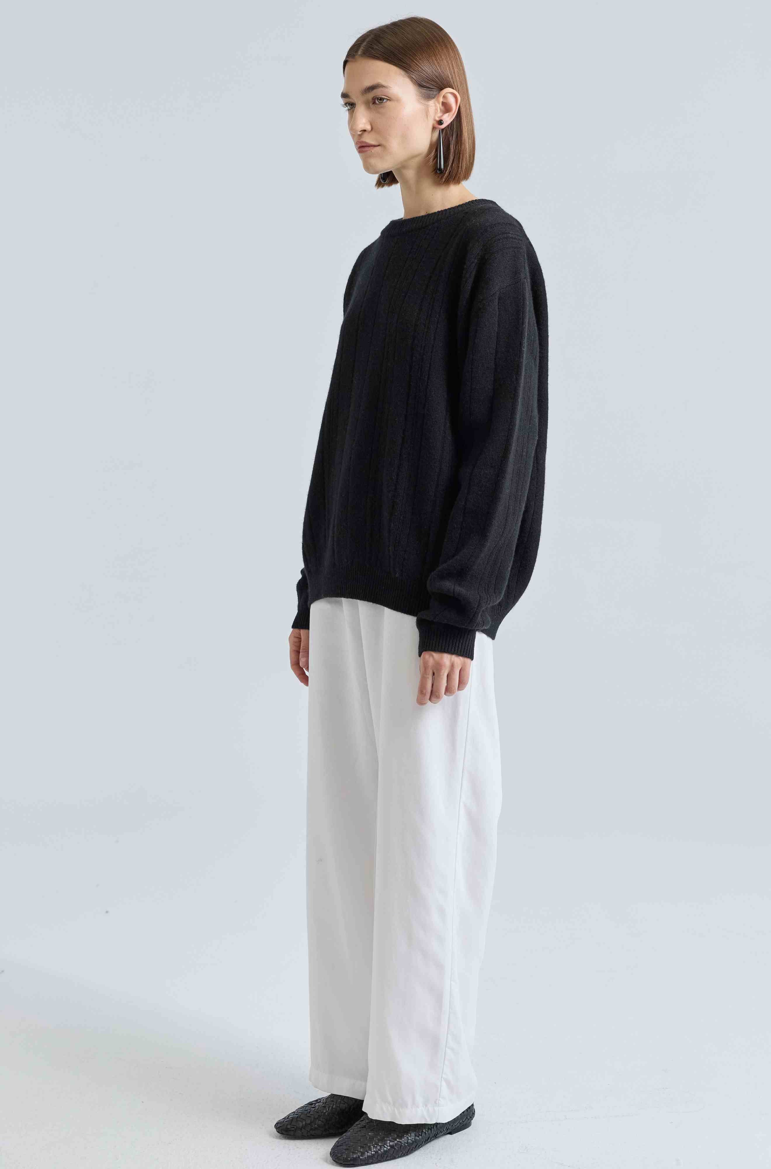 Person wearing a black sweater and white pants on a light gray background
