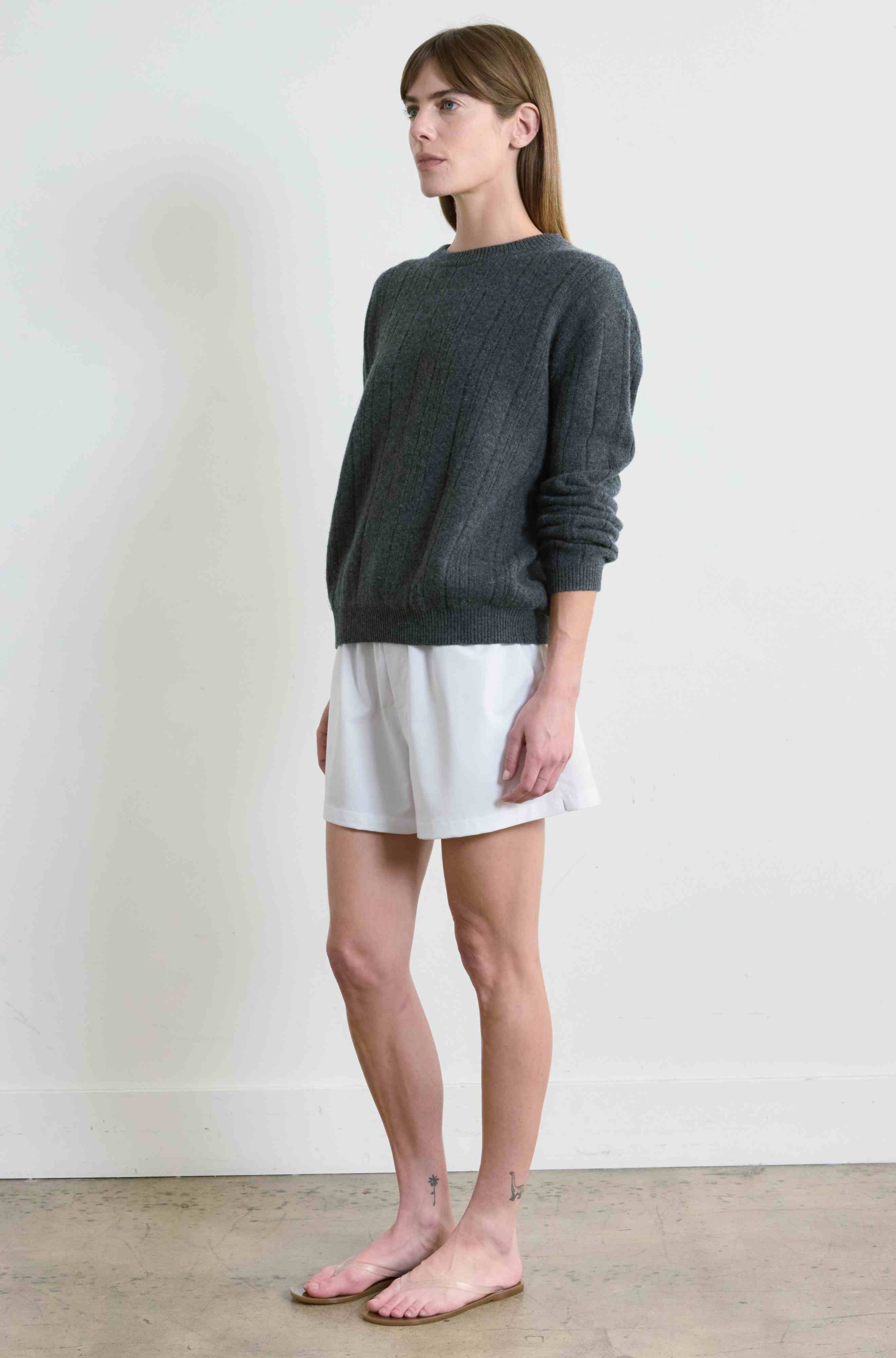 Woman wearing a dark gray sweater and white shorts against a plain background