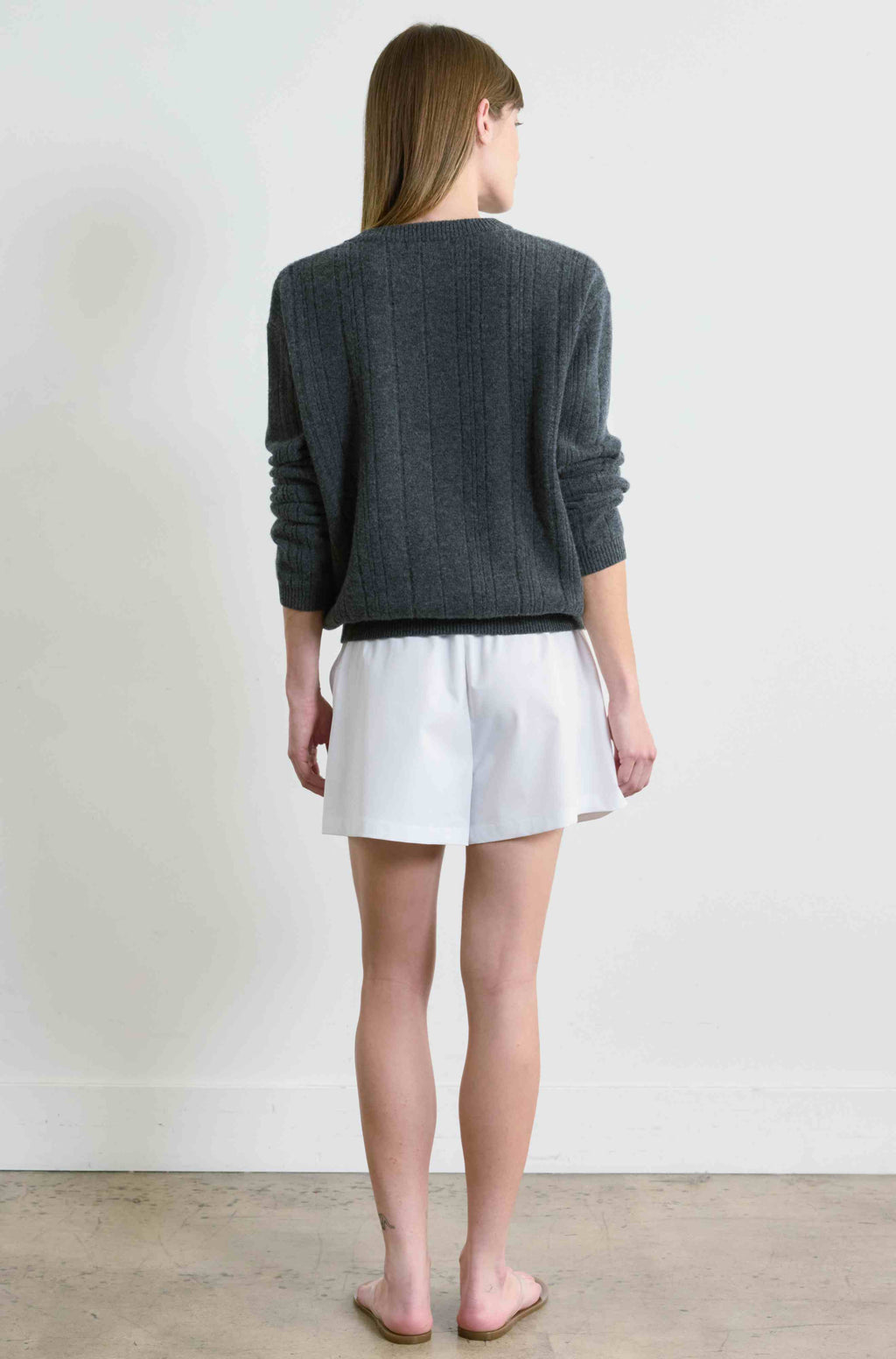 Person wearing a gray sweater and white shorts standing against a plain white wall.