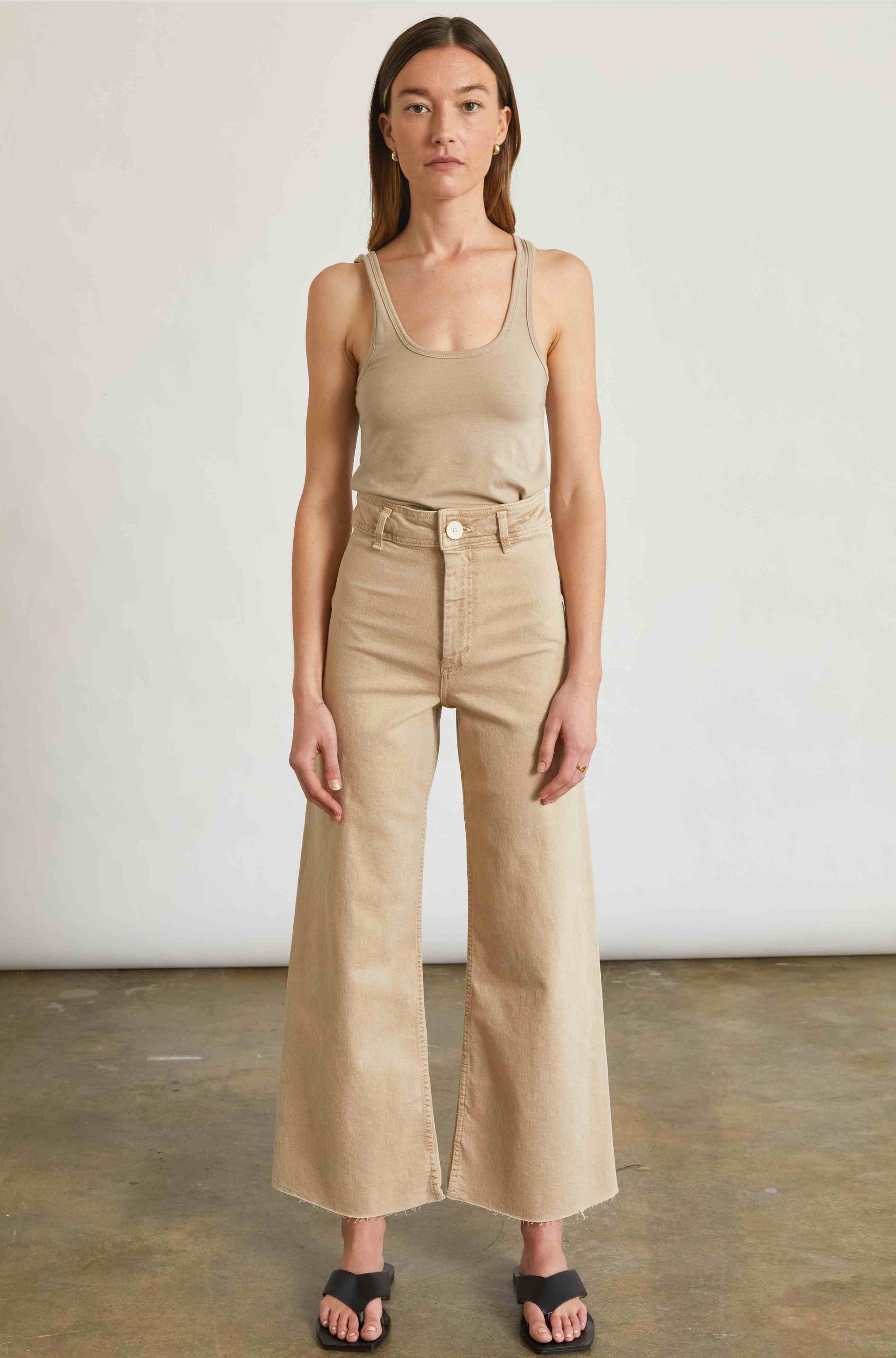 Woman wearing a beige tank top and wide-leg pants against a plain background