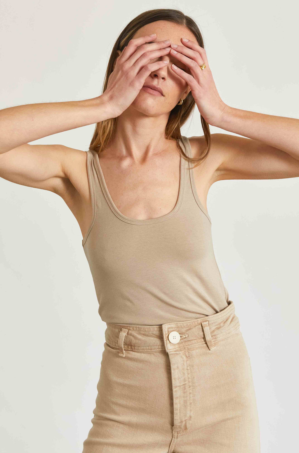 Woman wearing a beige tank top and pants against a plain background