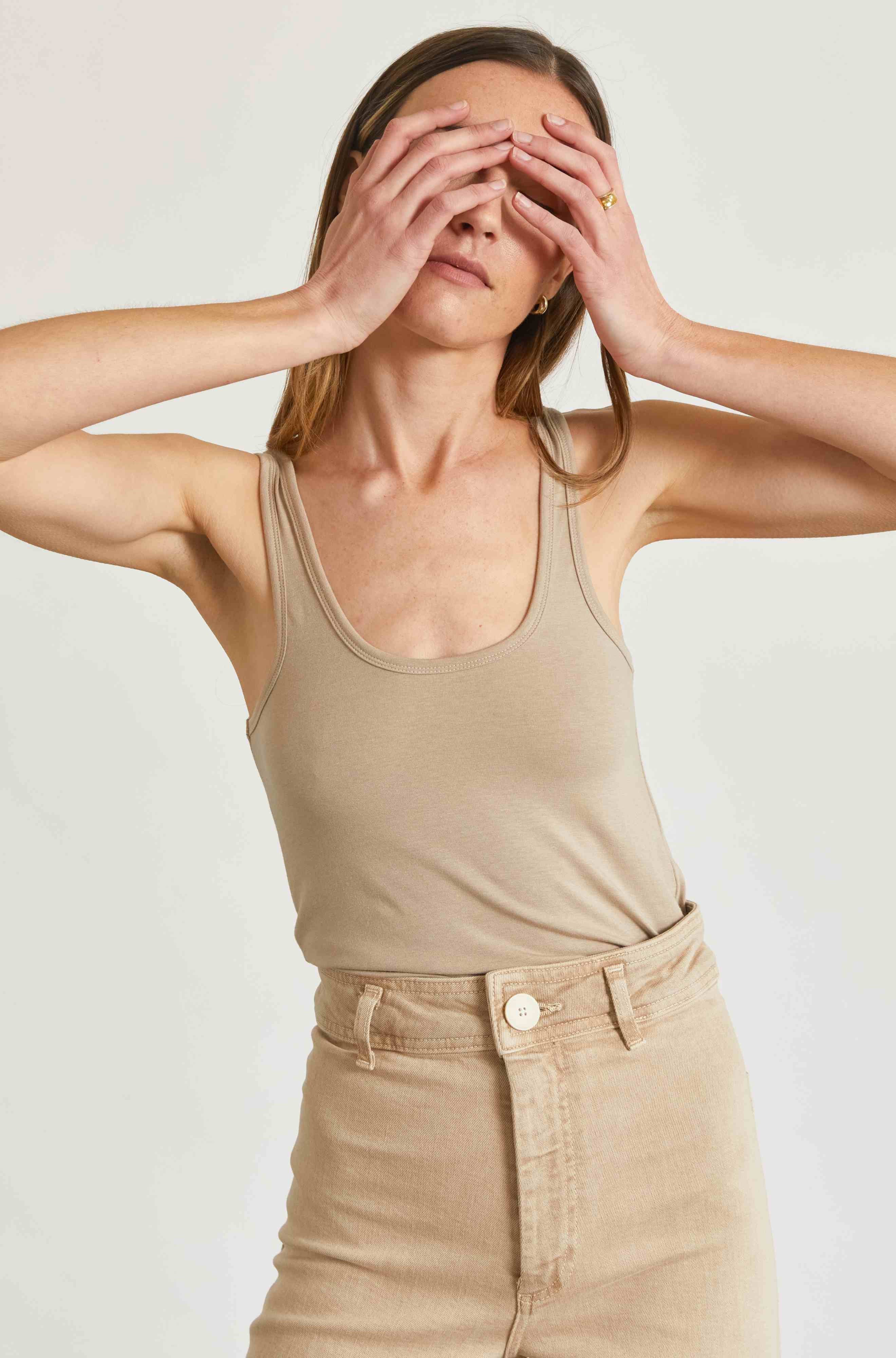 Woman wearing a beige tank top and pants against a plain background