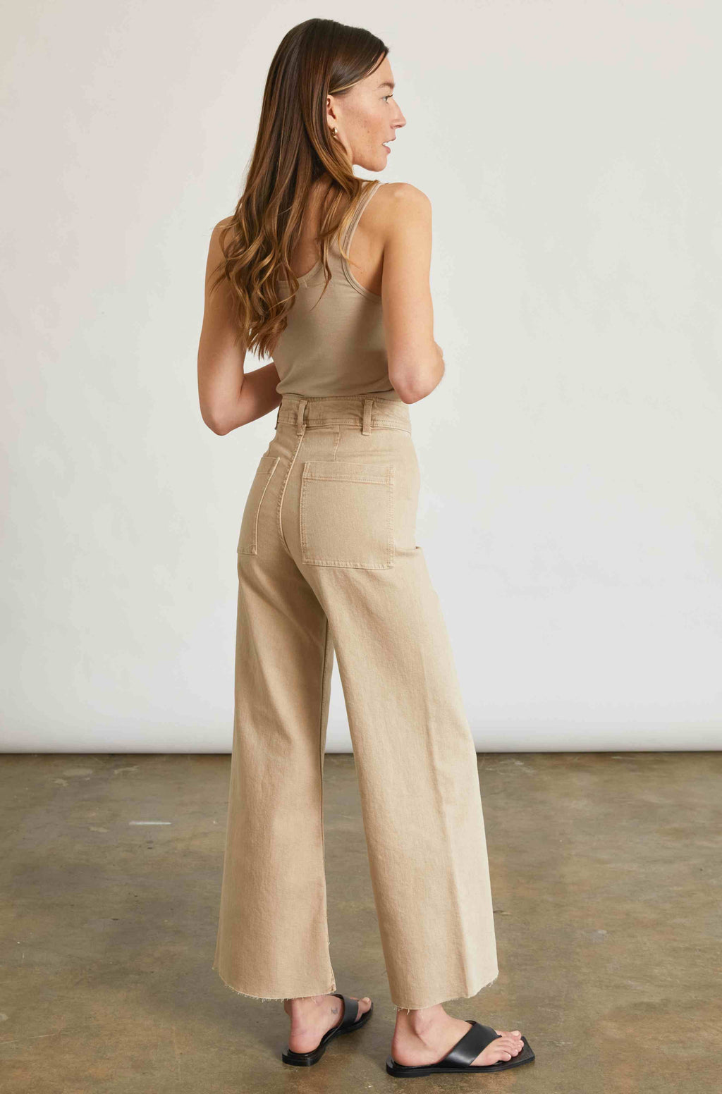 Woman wearing a beige jumpsuit standing against a plain background