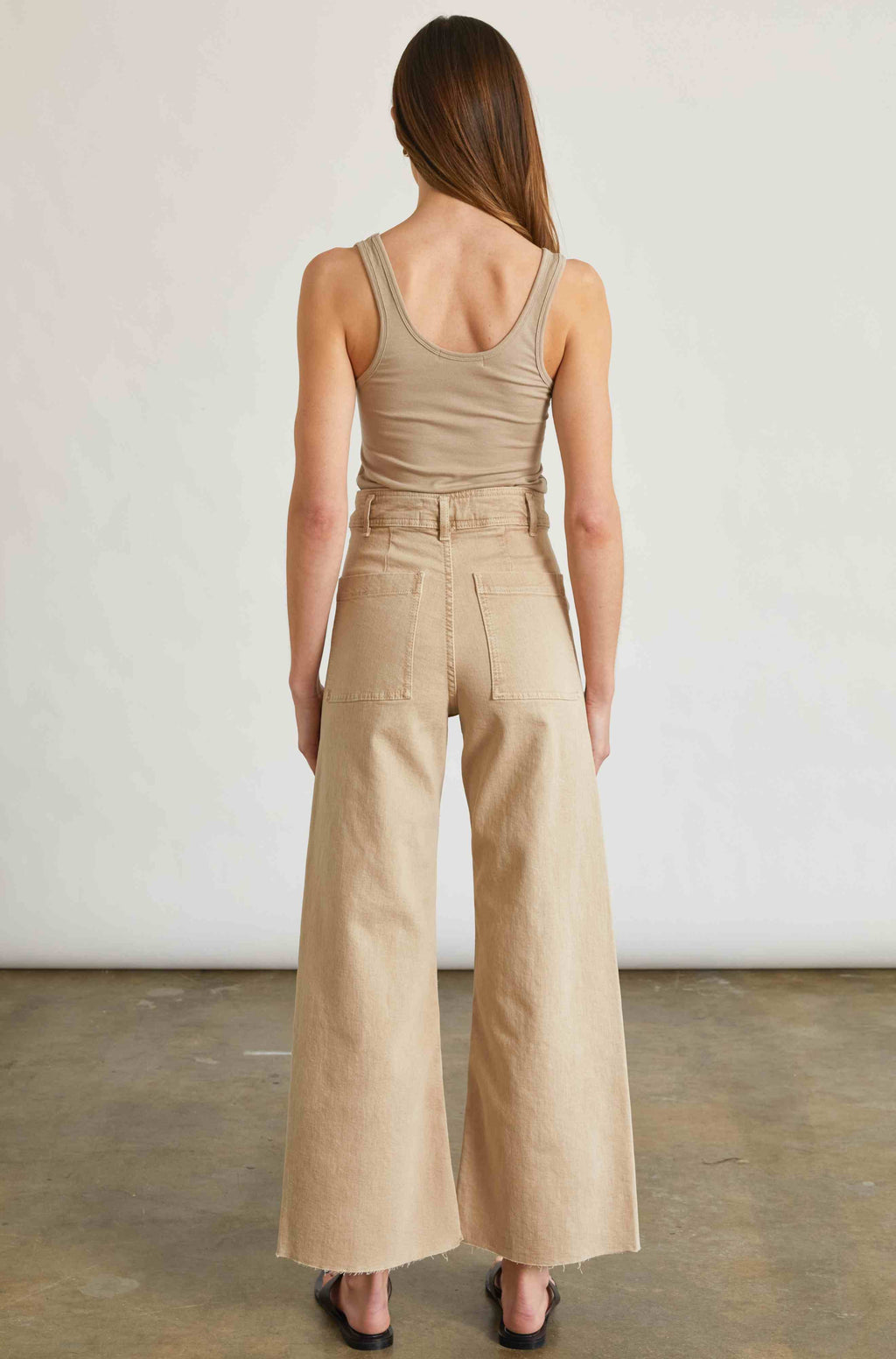 Woman wearing a beige shirt and pants standing against a plain background