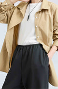 Person wearing a beige button up shirt over a white t-shirt and black pants on a light gray background