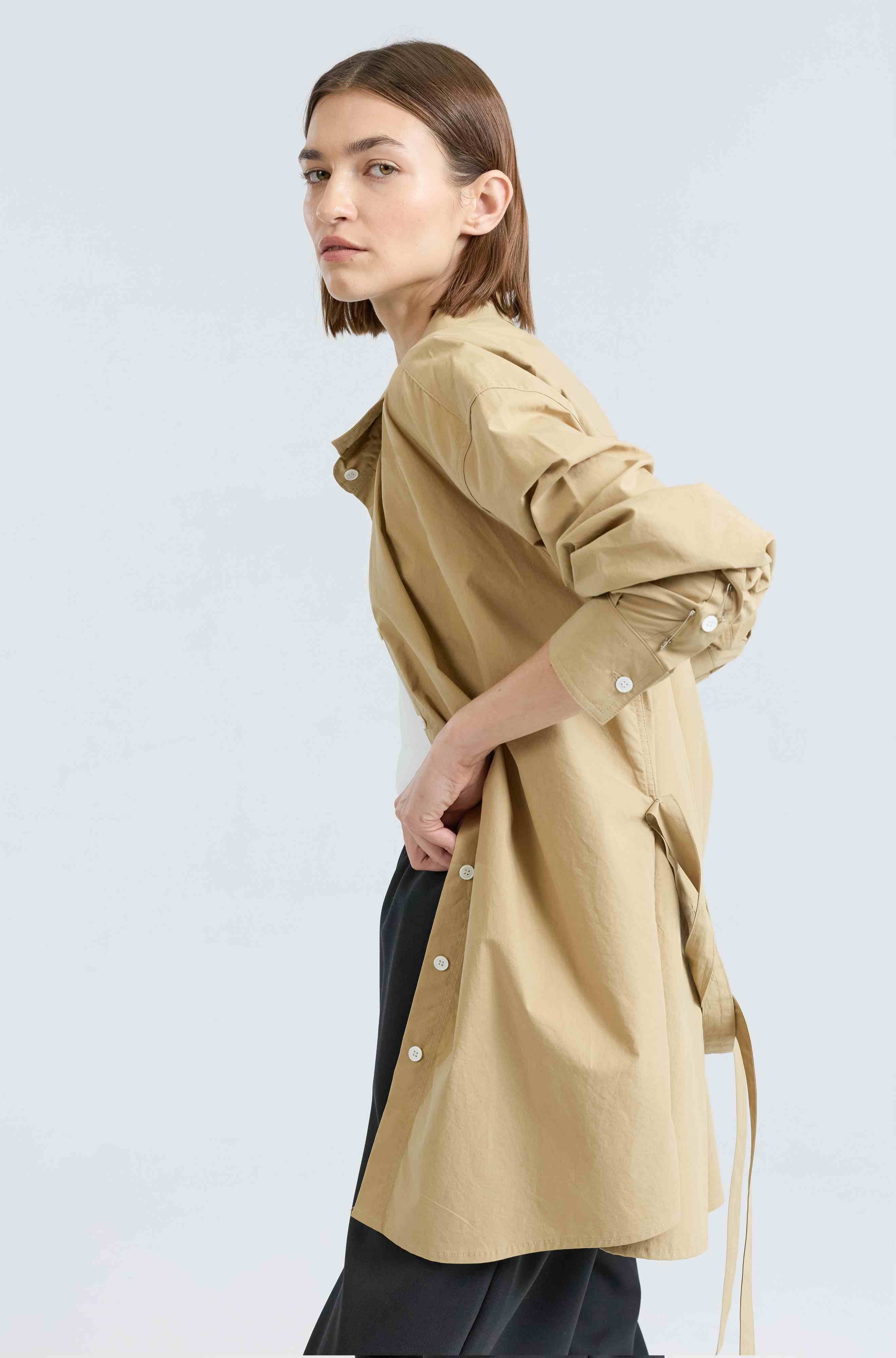 Woman wearing a beige button up shirt on a light gray background