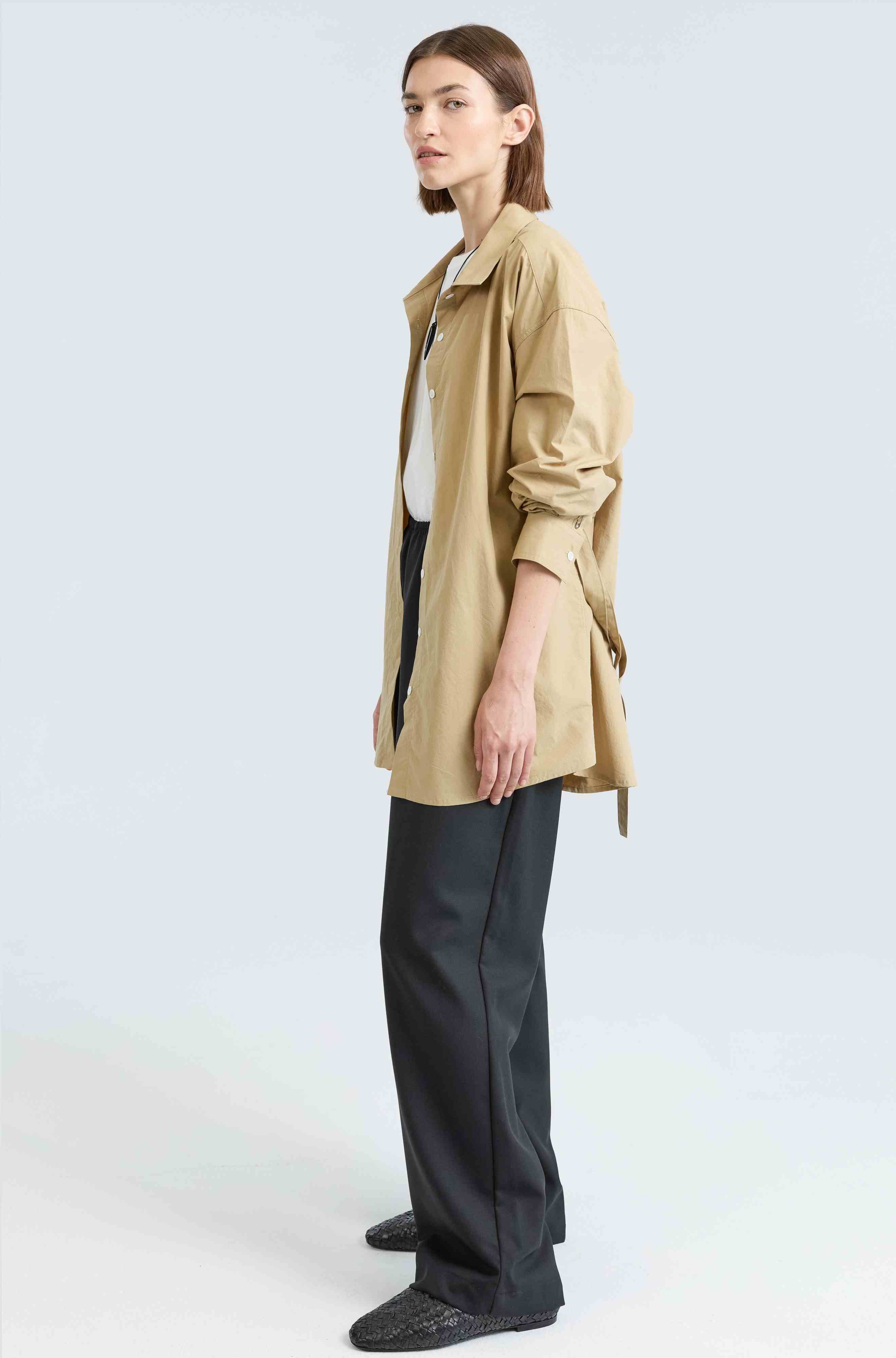 Woman wearing a beige shirt and black pants on a white background
