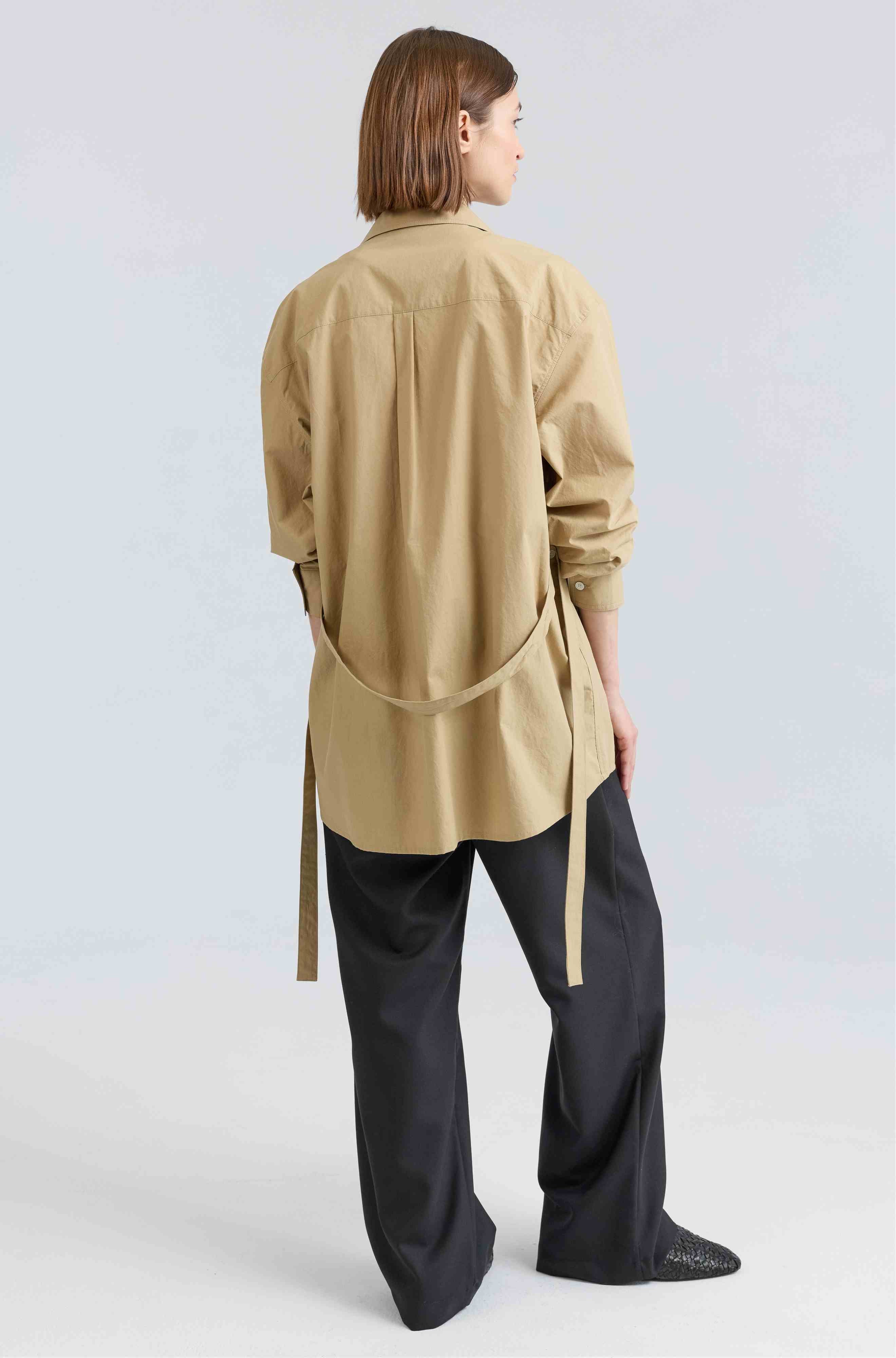 Person wearing a beige button up shirt and black pants on a light gray background