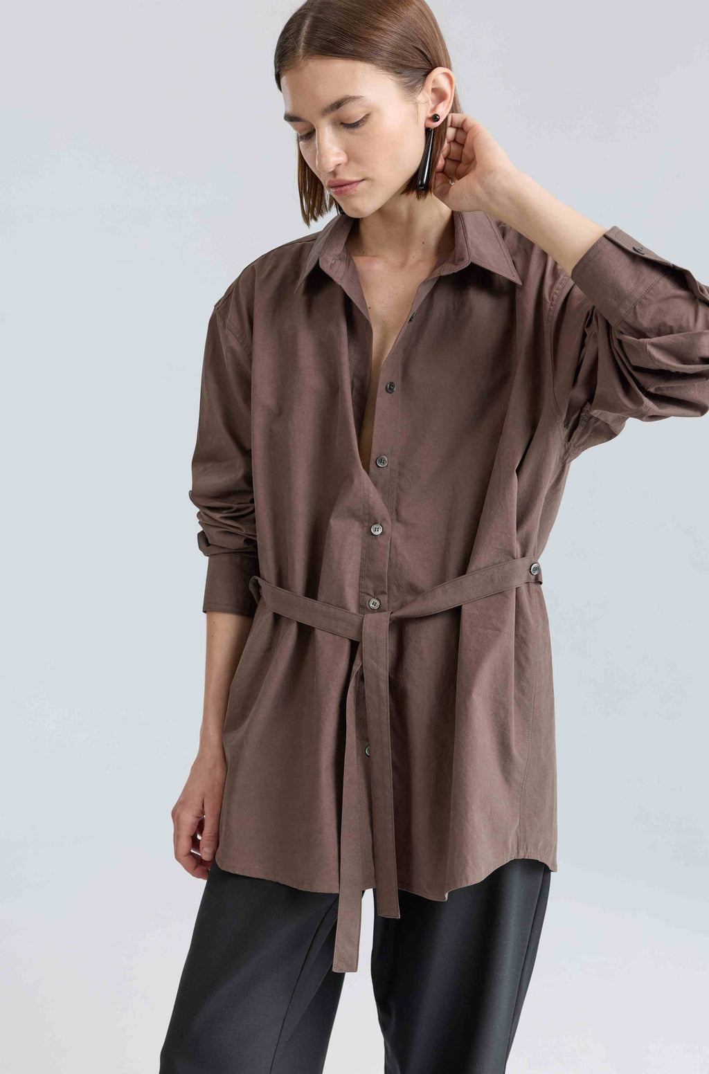 Woman wearing a brown button-up shirt with a belt on a light gray background