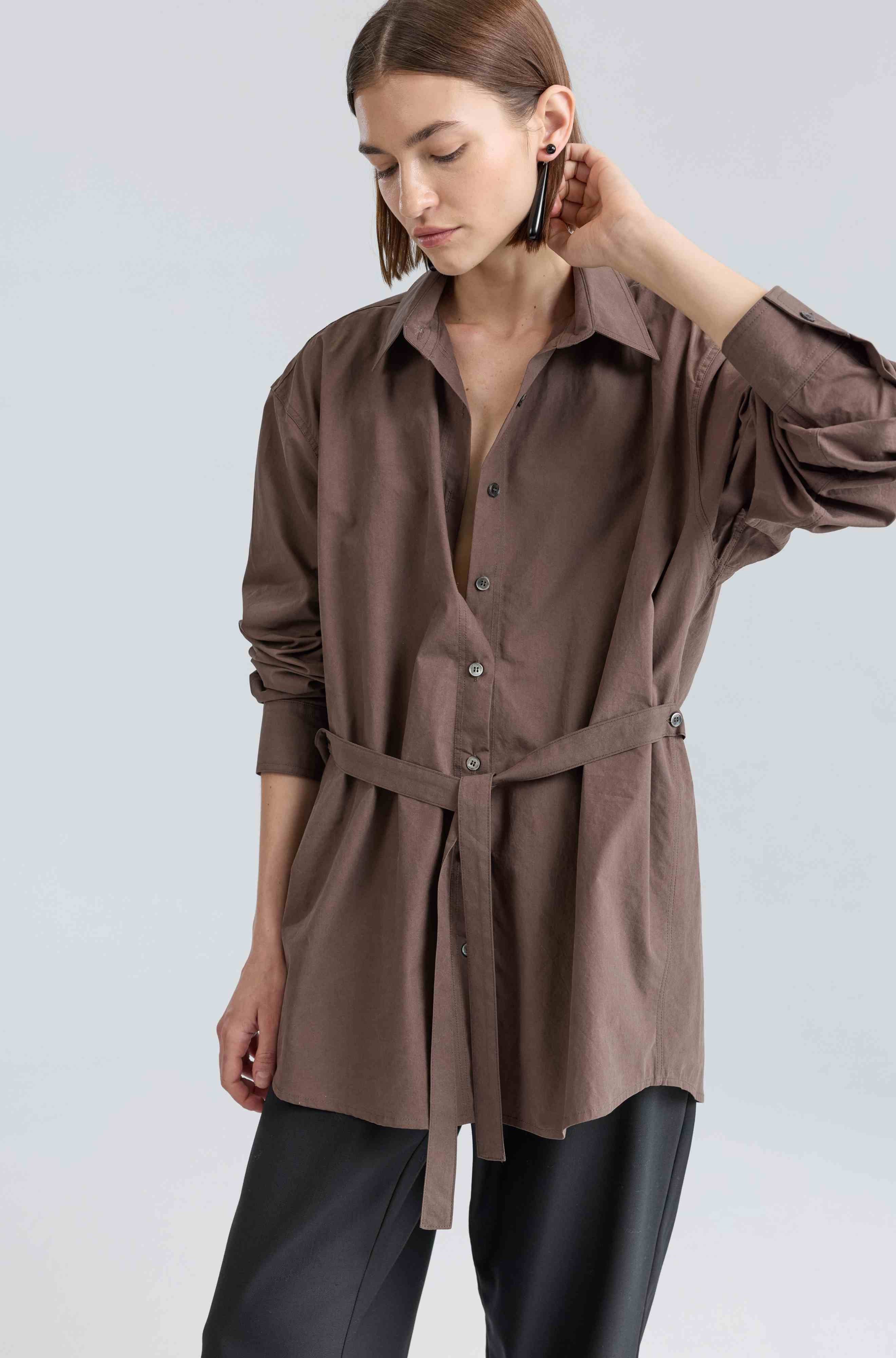 Woman wearing a brown button-up shirt with a belt on a light gray background