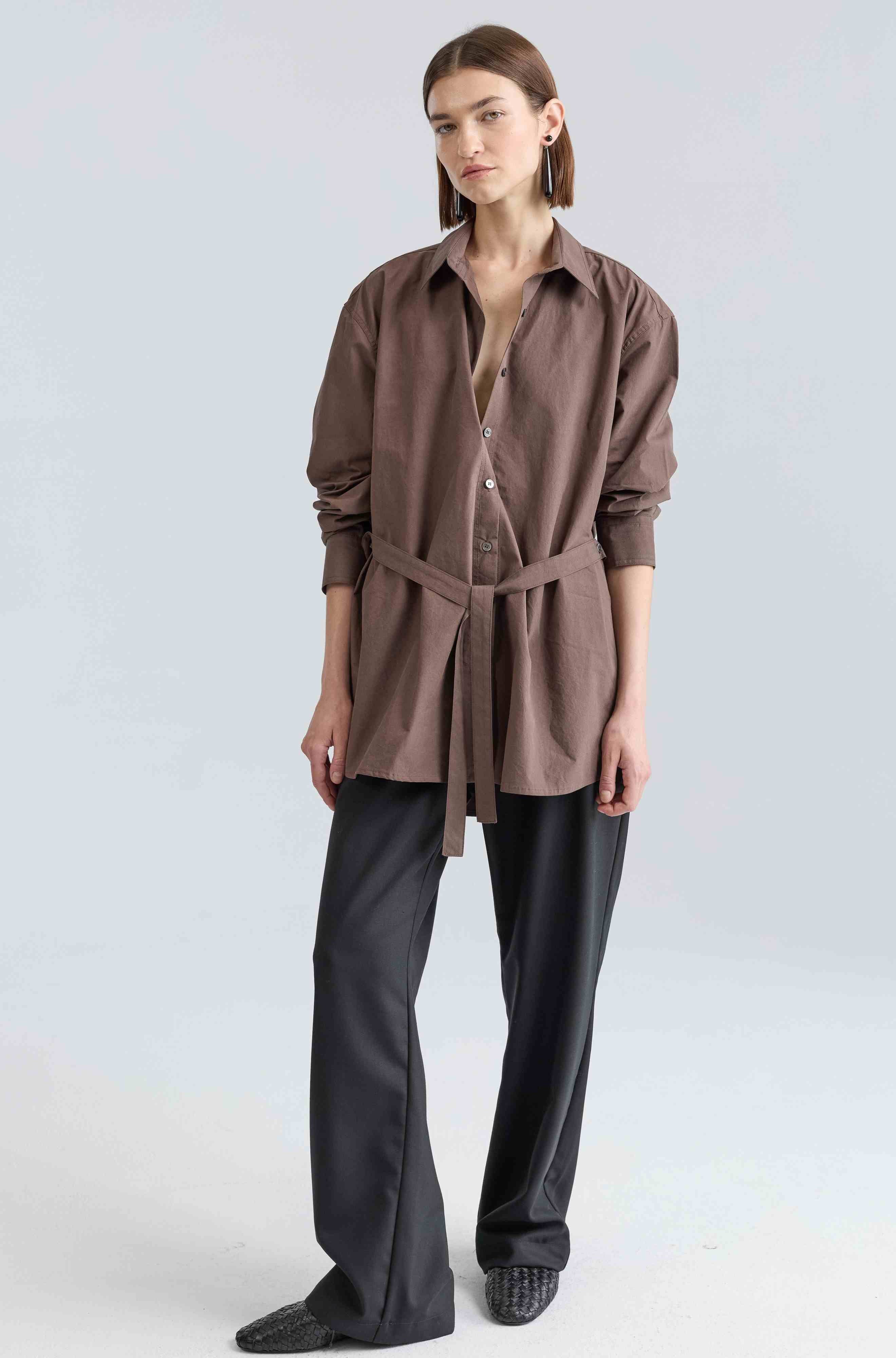 Woman wearing a brown shirt and black pants on a light gray background