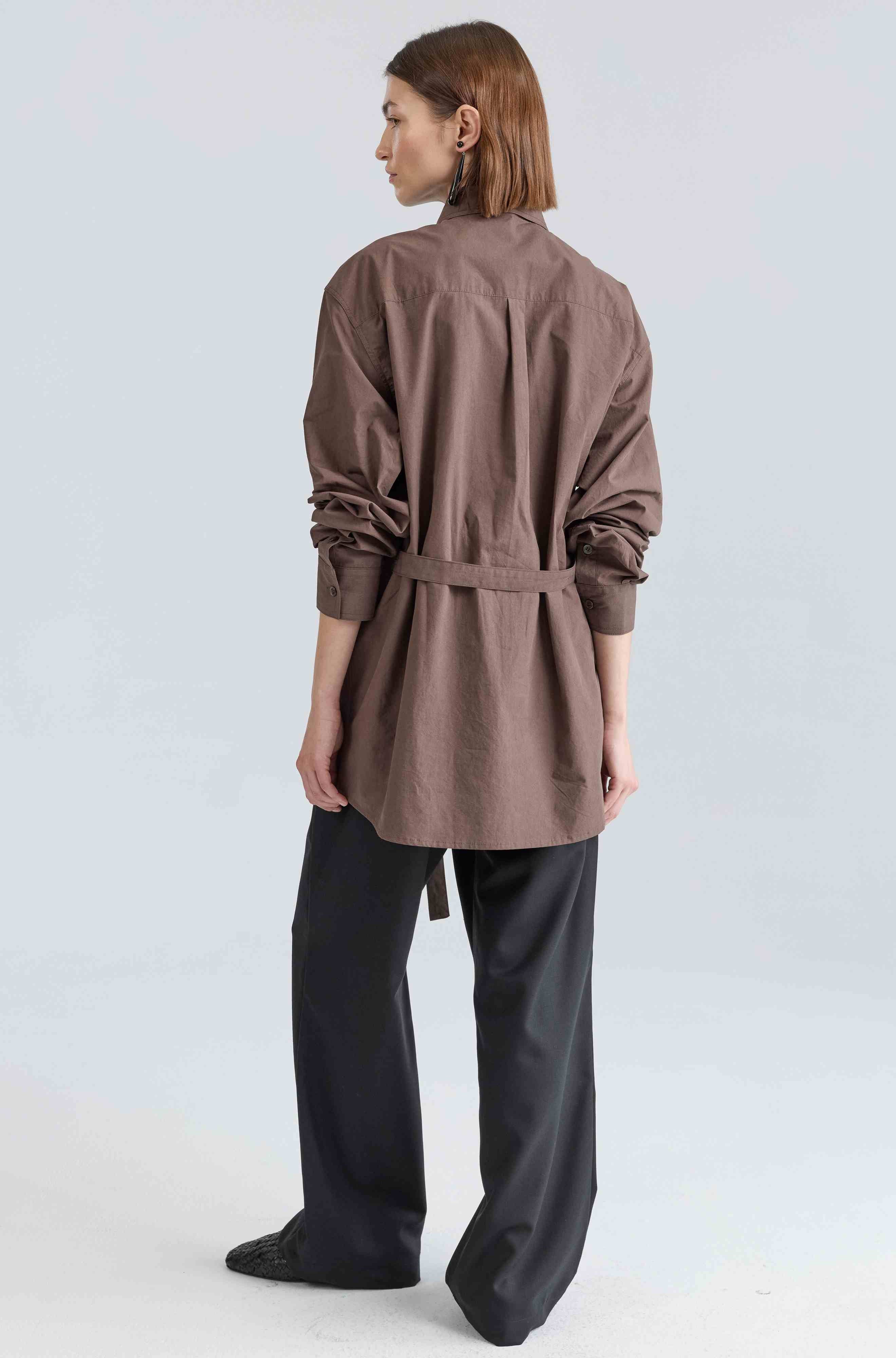 Person wearing a brown long-sleeve shirt and black pants on a light gray background