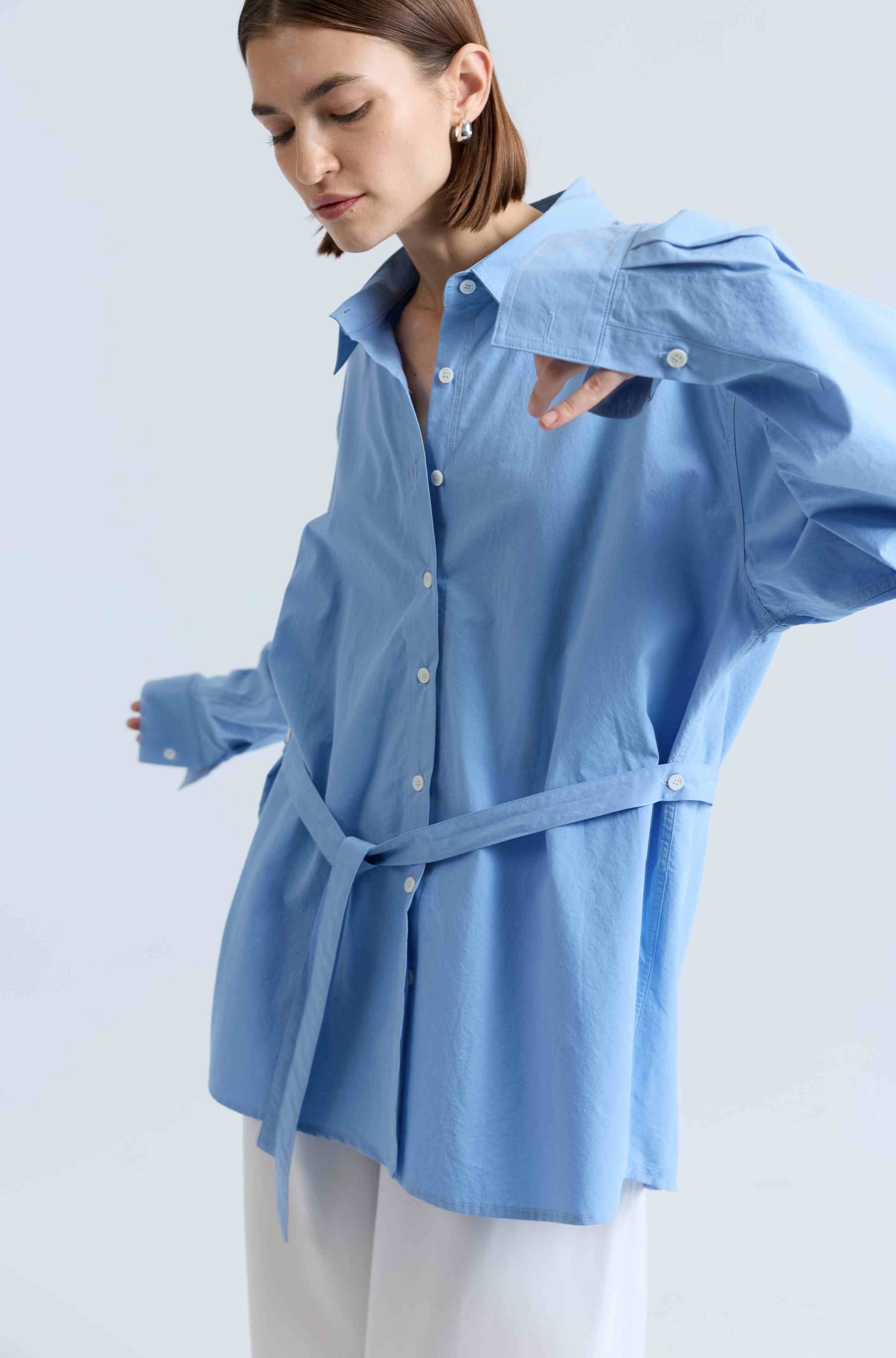 Woman wearing a light blue shirt with a belt against a white background
