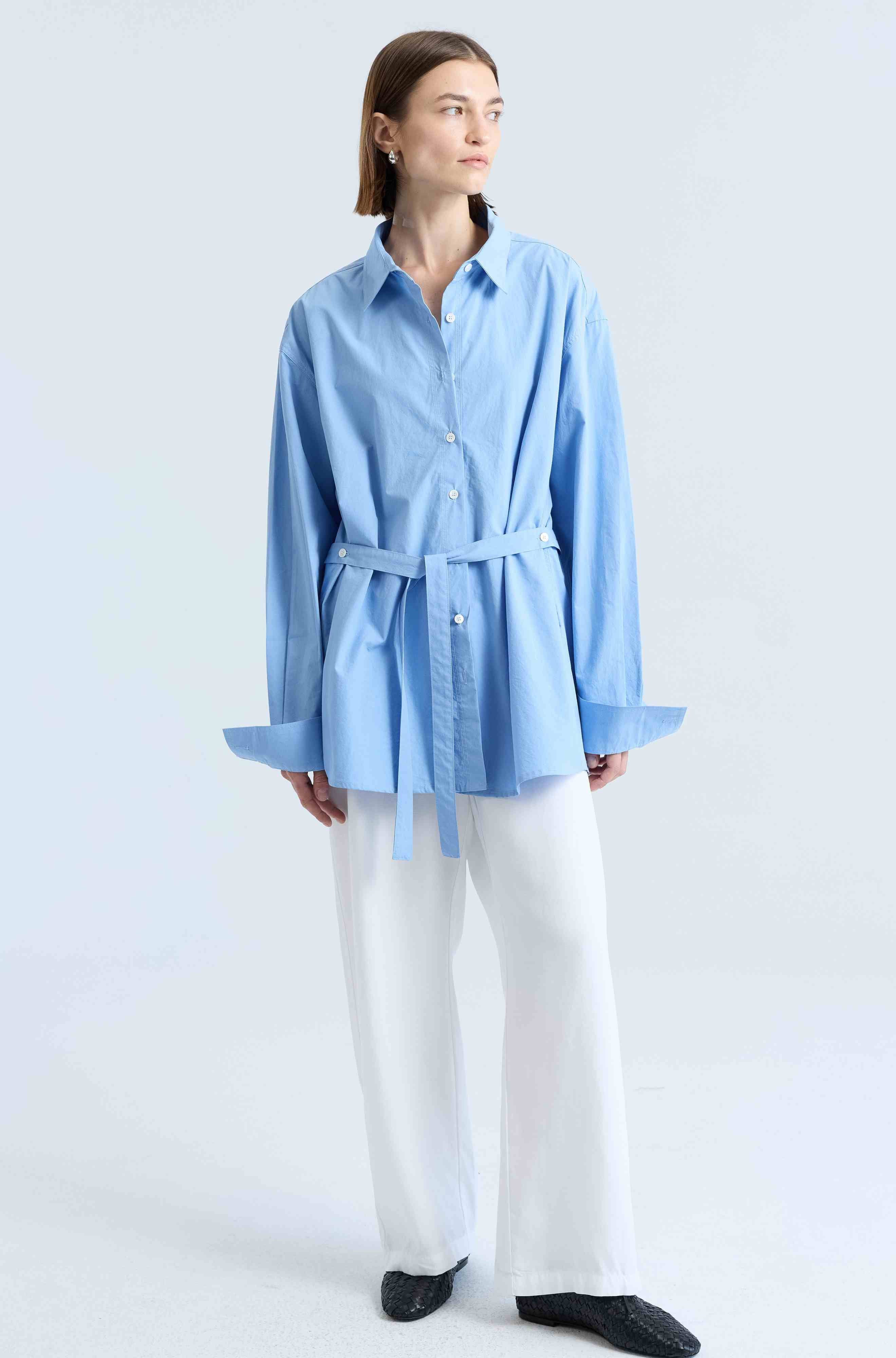 Person wearing a light blue shirt and white pants on a white background