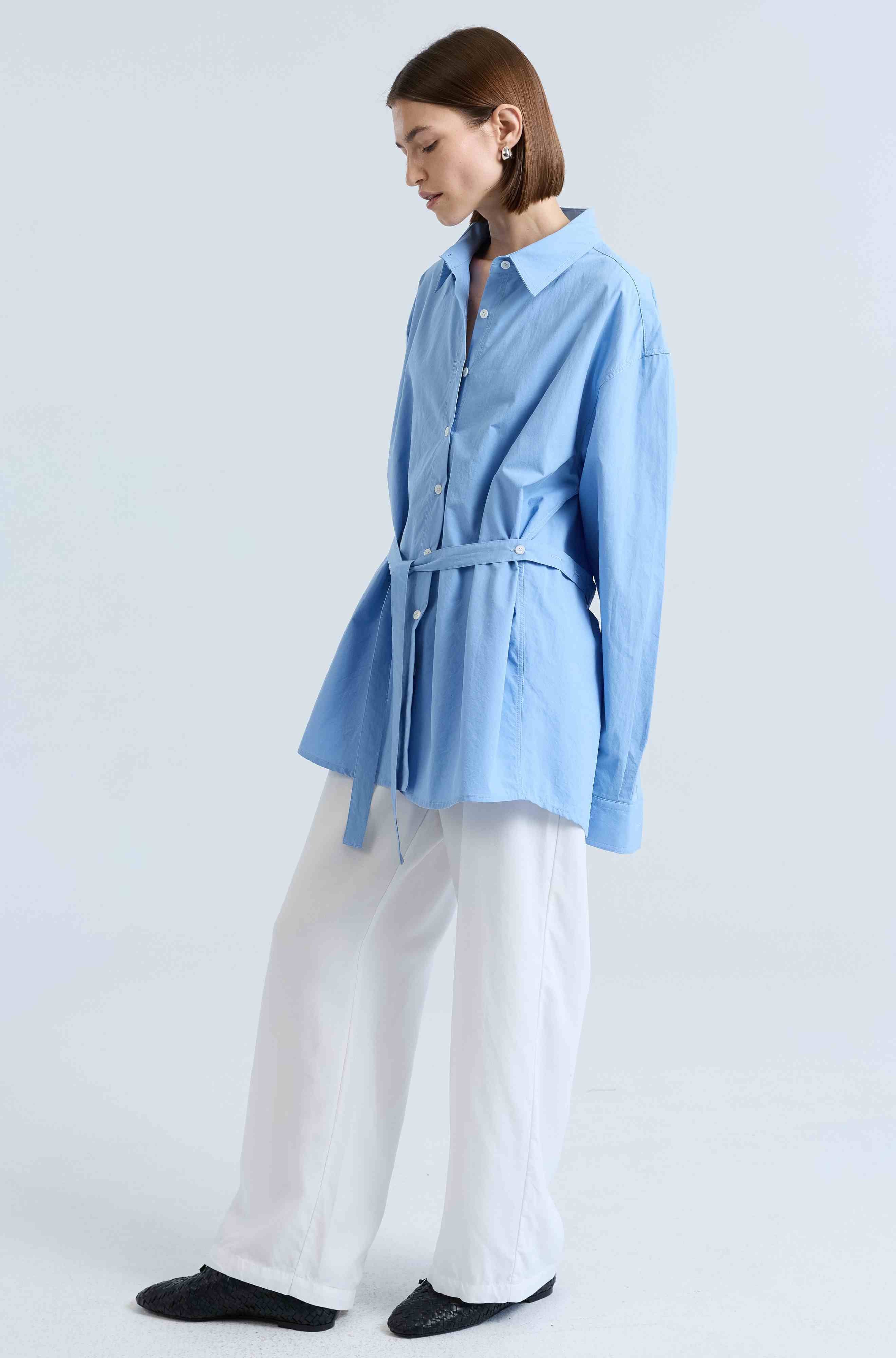 Woman wearing a light blue shirt and white pants on a plain background