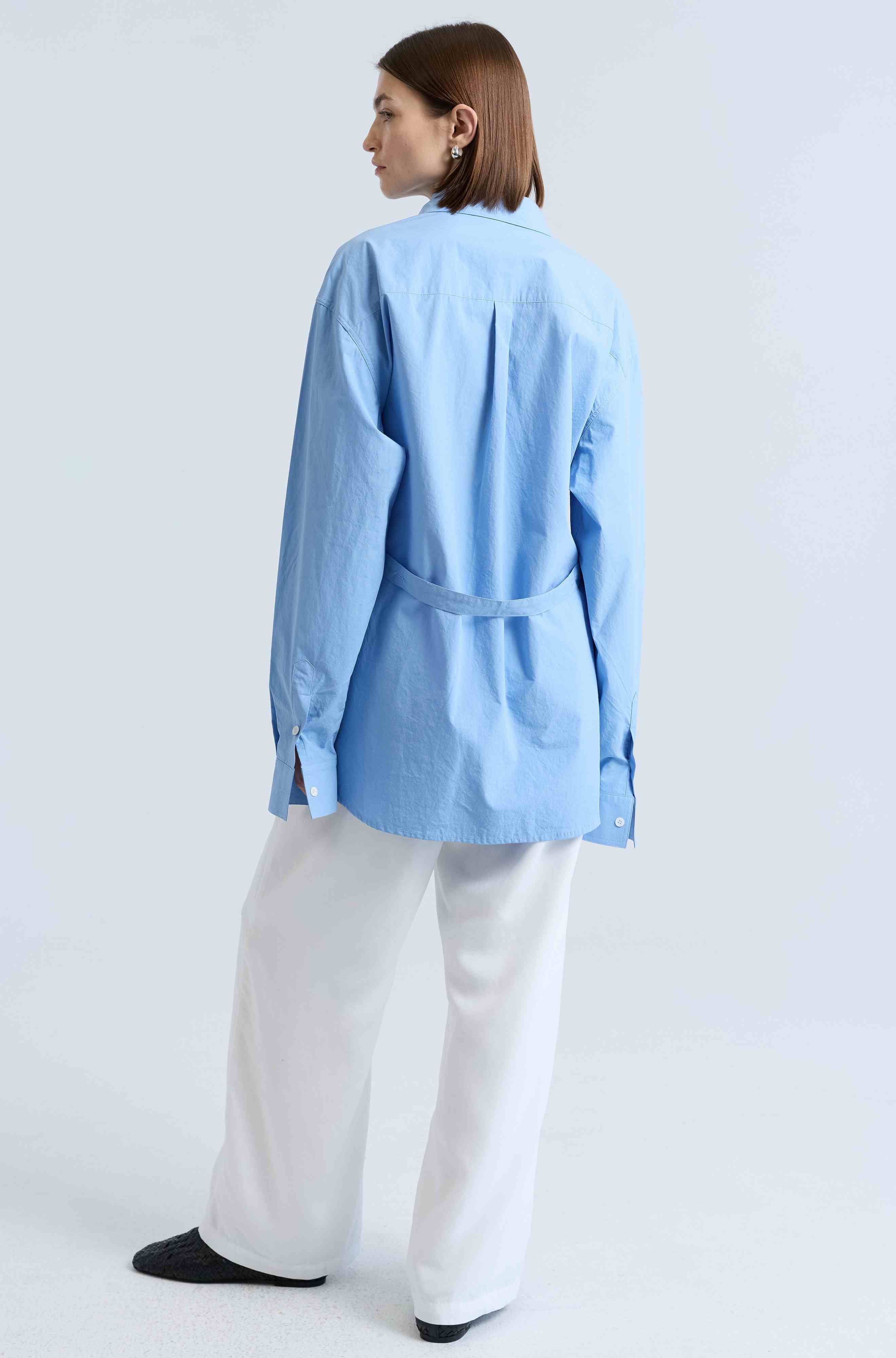 Person wearing a light blue shirt and white pants on a white background