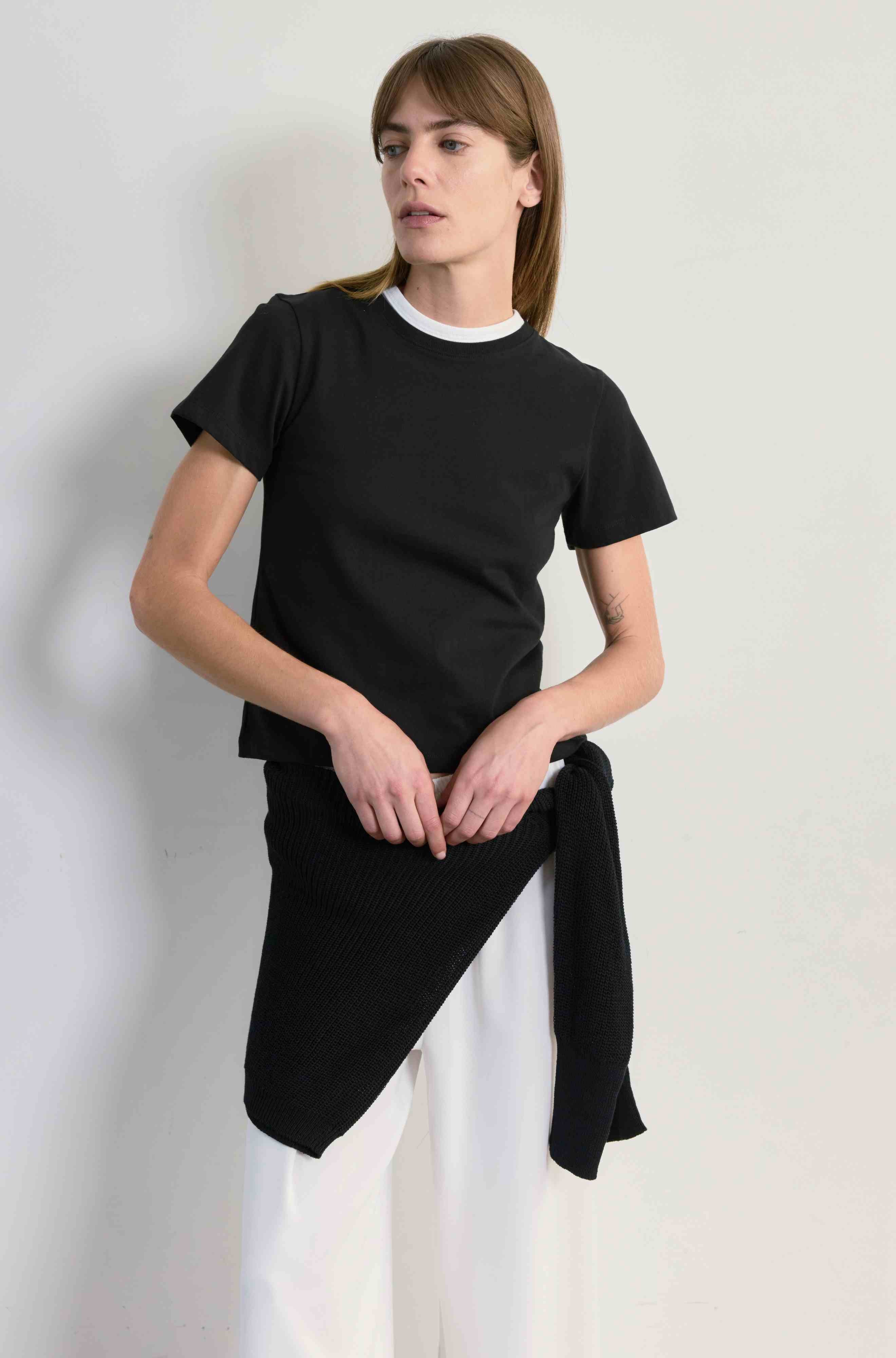 Person wearing a black t-shirt with an asymmetrical hem against a plain background
