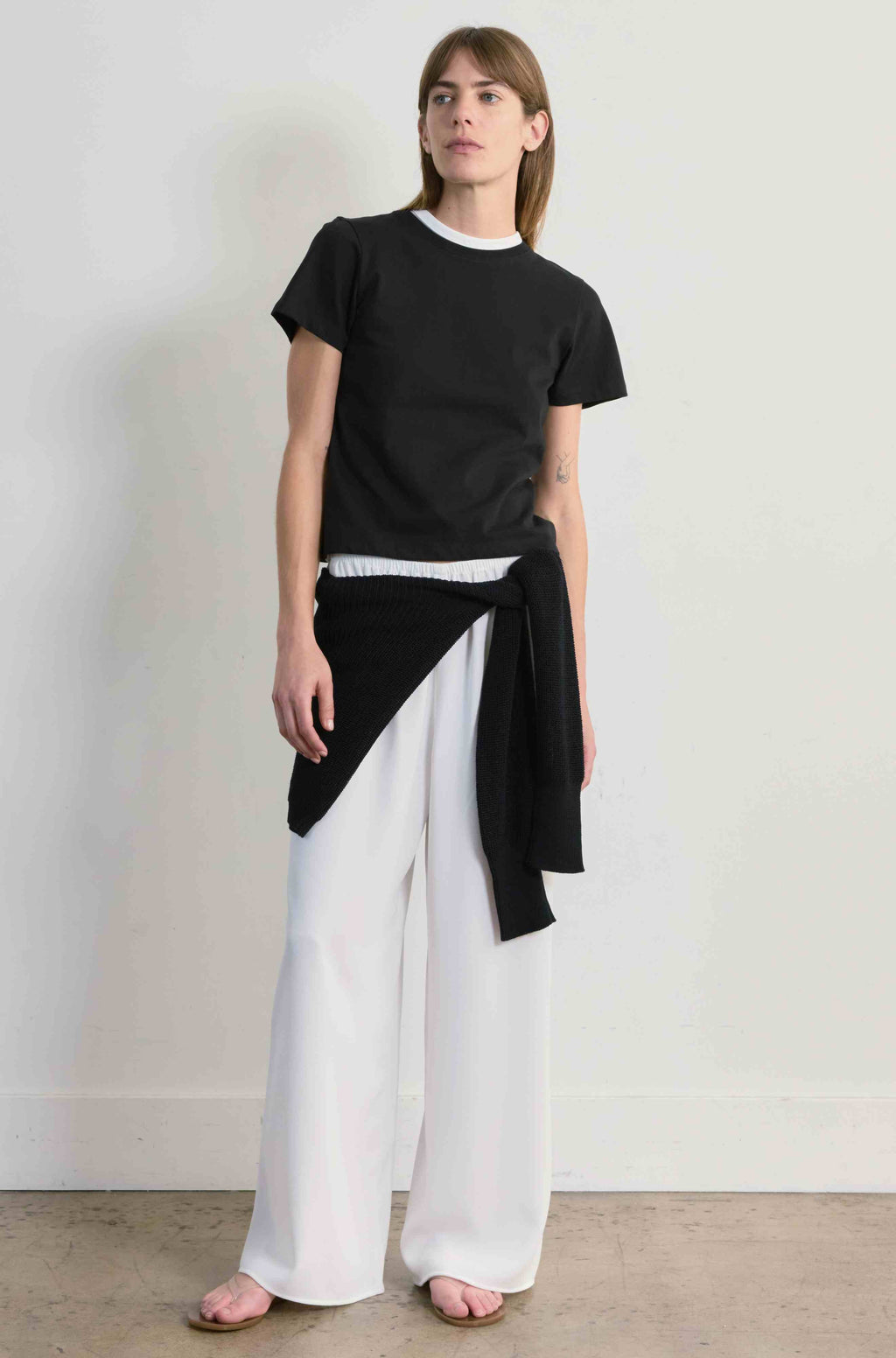 Woman wearing a black top and white pants against a plain background